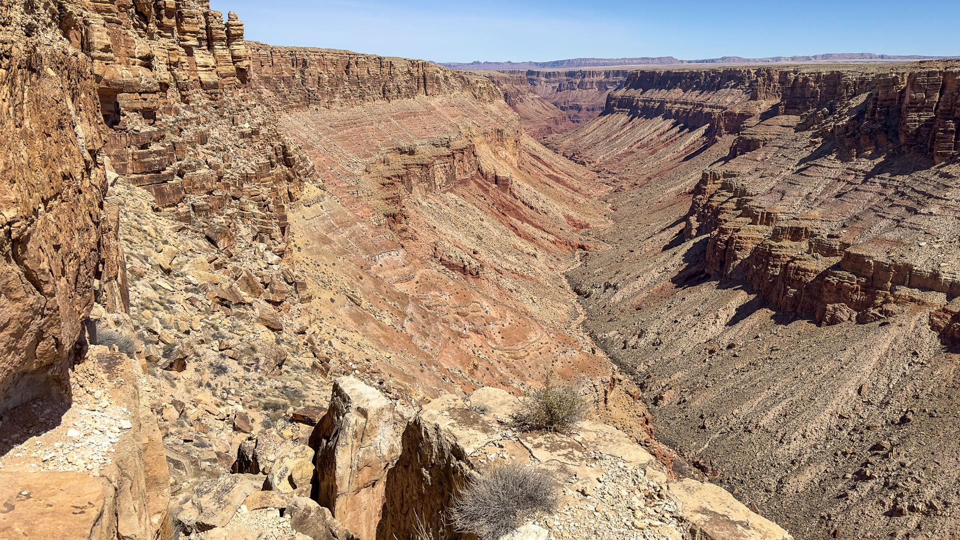 A deep canyon with reddish-brown rock formations under a clear blue sky.