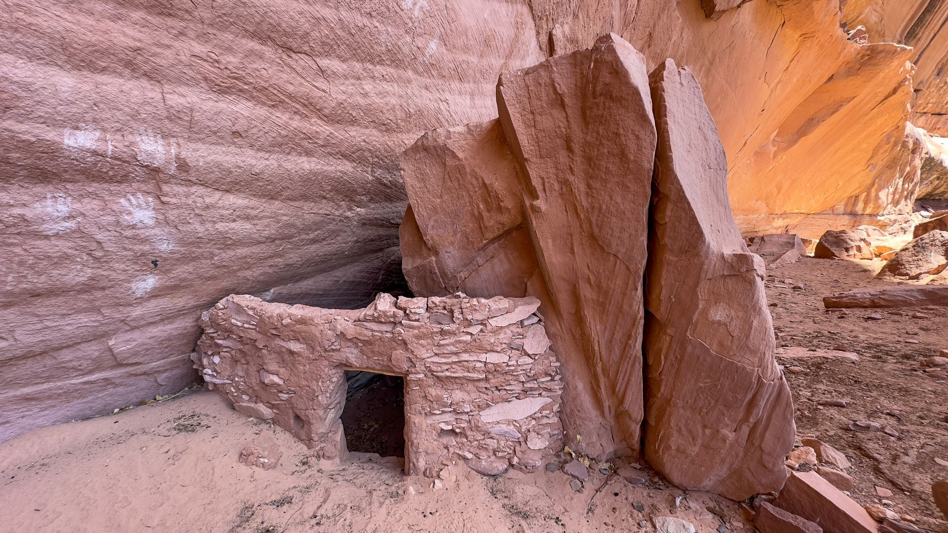 Ancient stone dwelling built into a sandstone cliff. Entrance doorway visible; tan and brown colors.