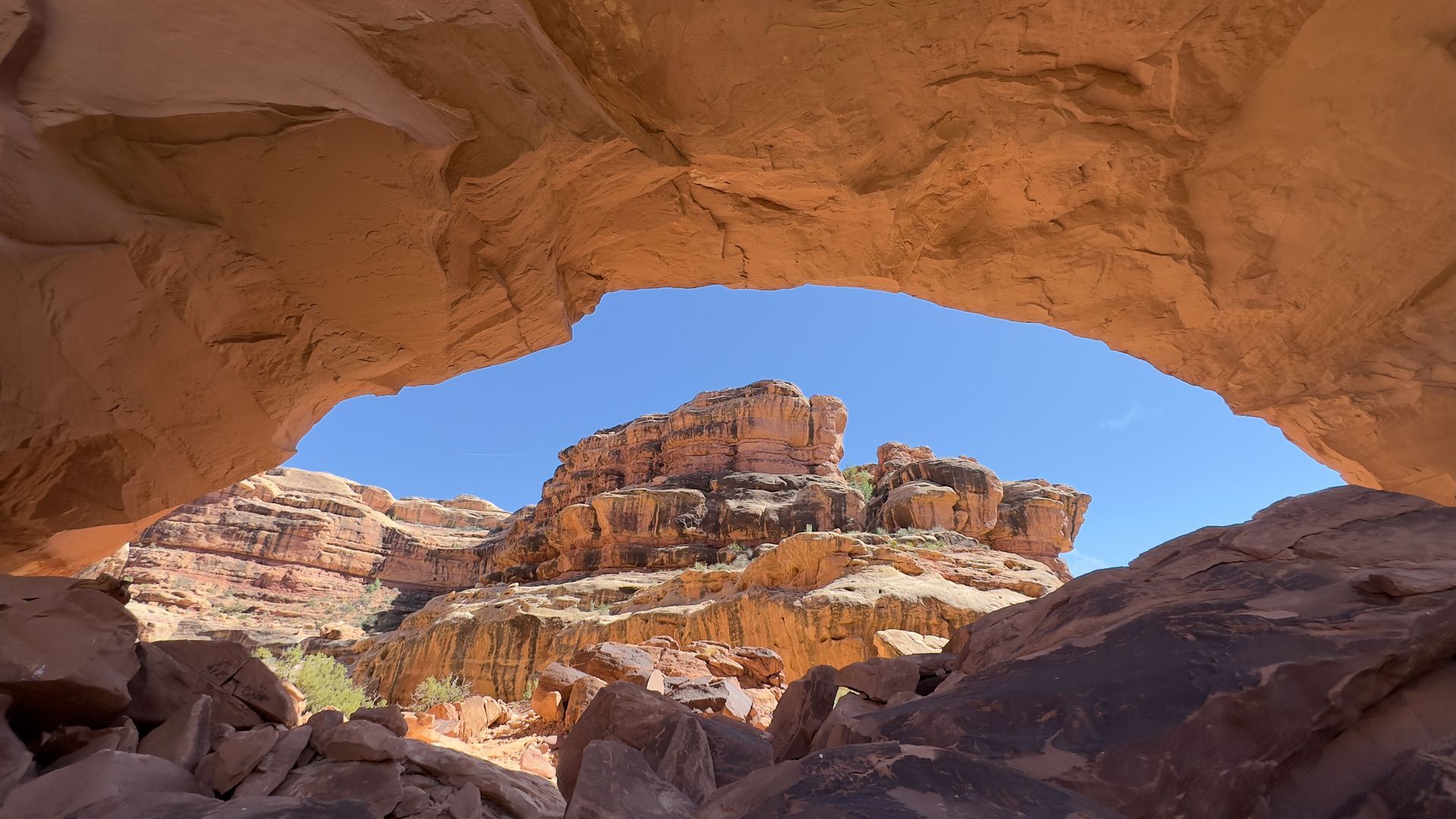 View through a rock archway of a desert landscape with red rock formations and a blue sky.