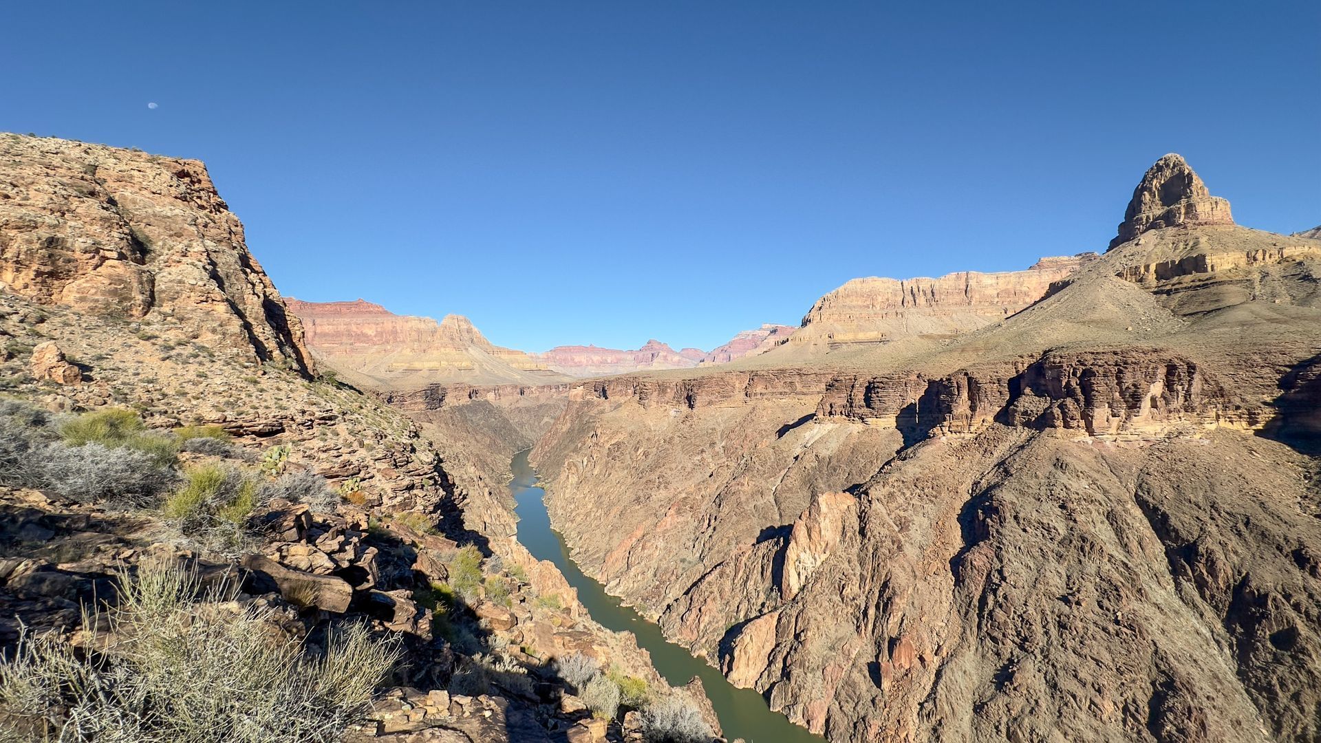 Grand Canyon vista, river winding through deep, brown-rock canyon under blue sky.