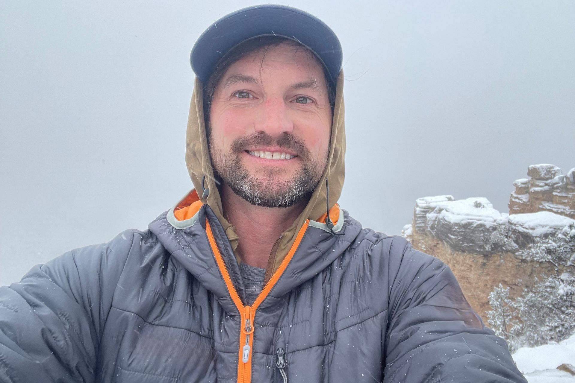 A man wearing a hat and a jacket is taking a selfie in the snow.