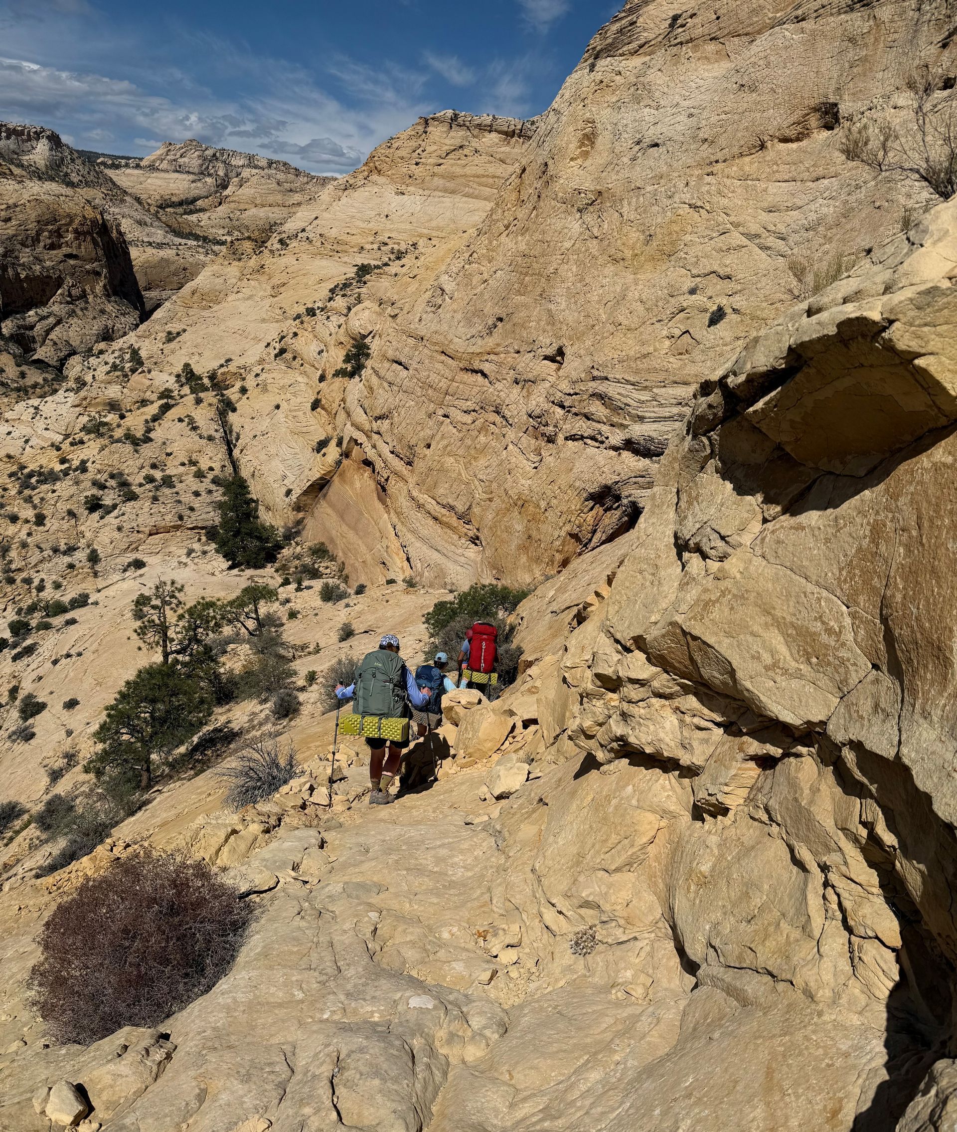 Hikers with packs ascend a rocky mountain trail, brown landscape, clear sky.