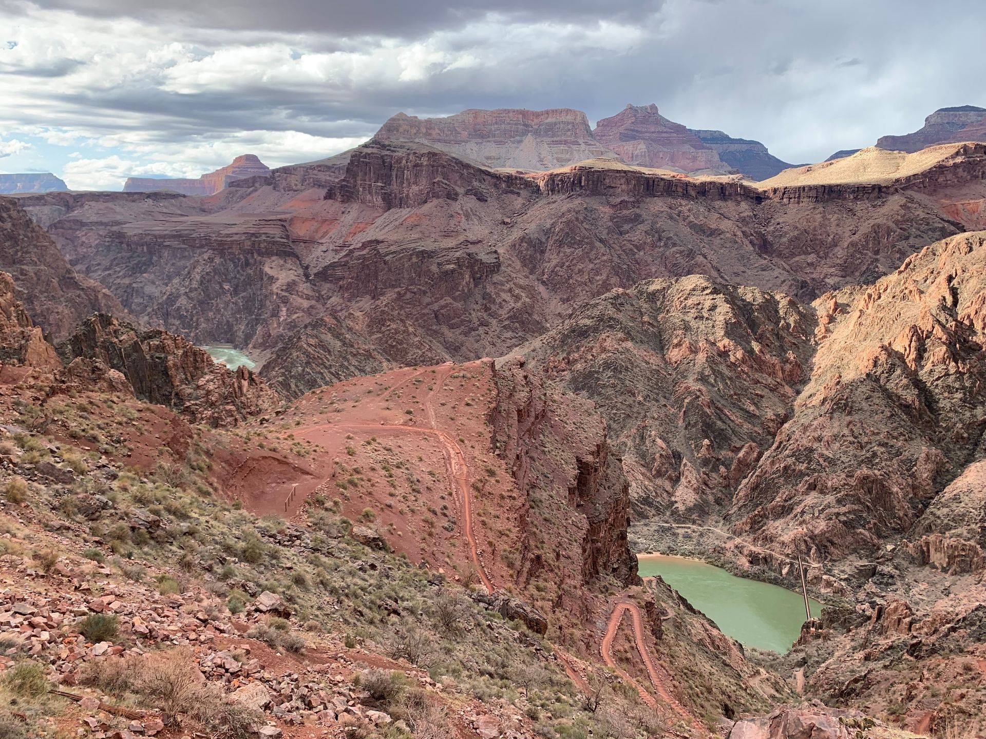 A view of a canyon with mountains in the background and a river in the middle.