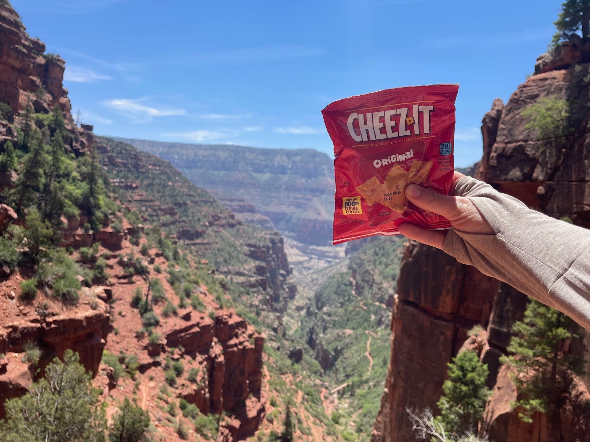 Hand holding a bag of Cheez-Its against a backdrop of a deep canyon with red rock formations.