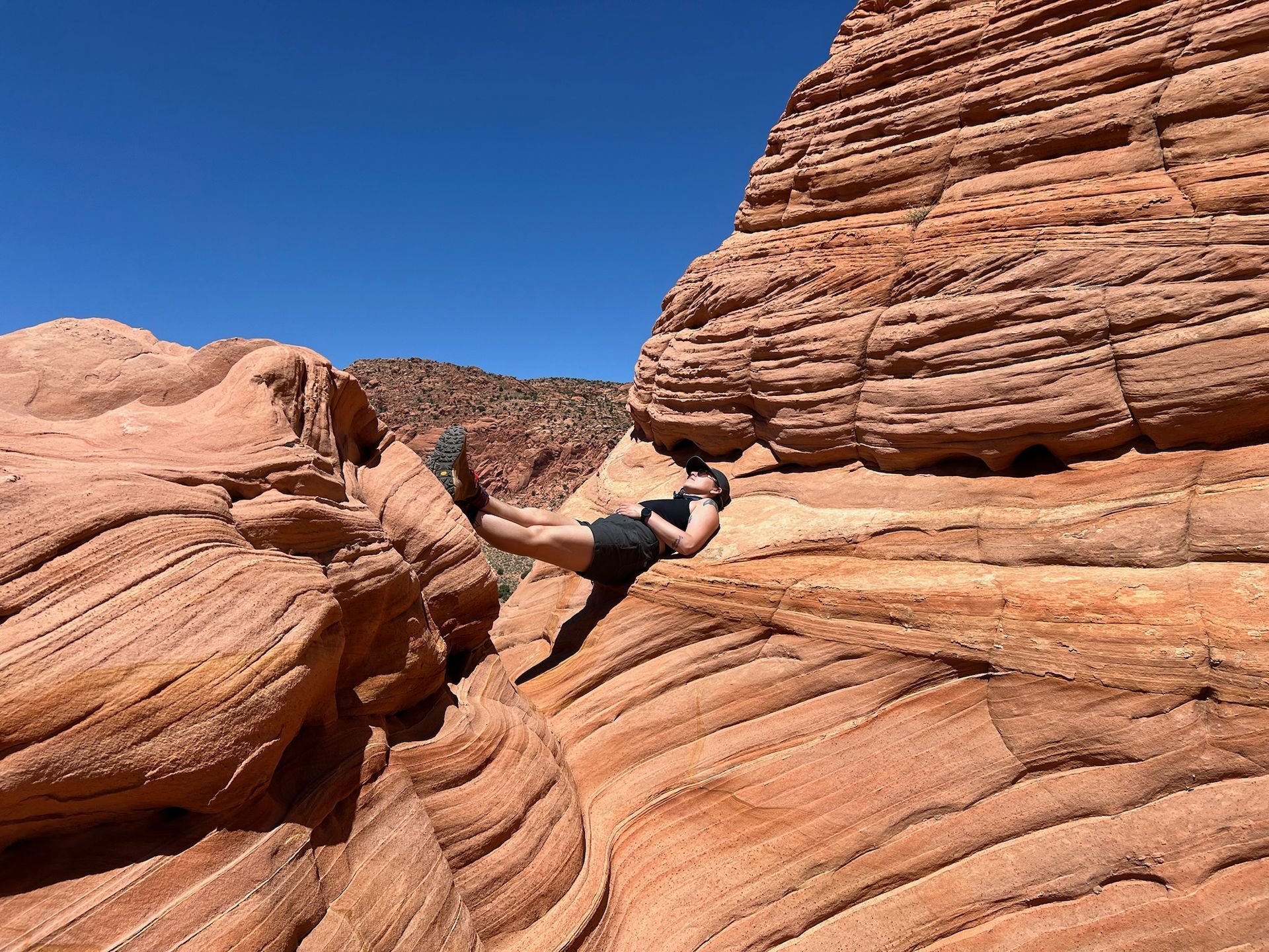 Person lying on red sandstone formations under a clear blue sky.
