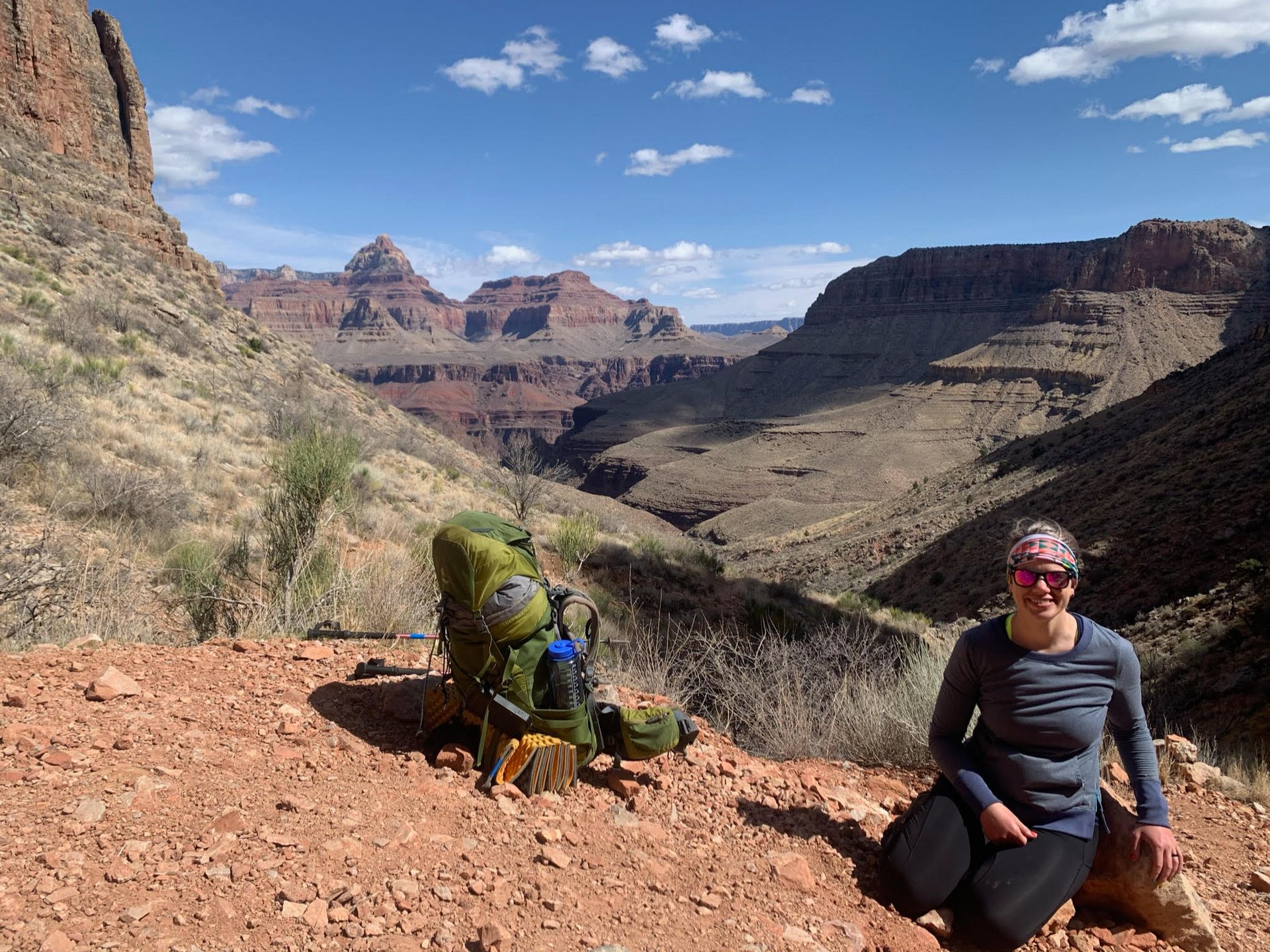 A woman is kneeling on the ground next to a backpack in a canyon.