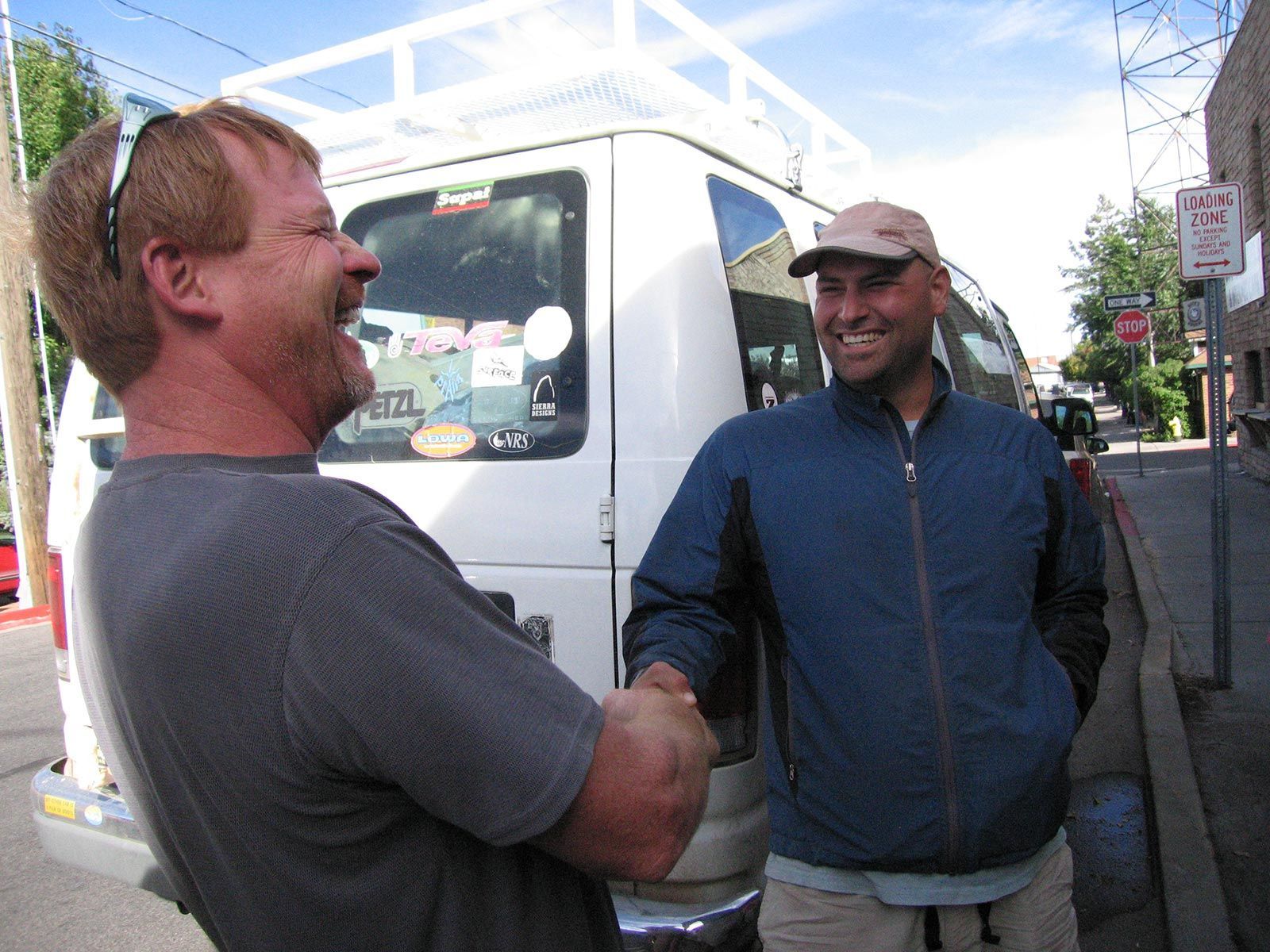 Two men shaking hands in front of a no parking sign