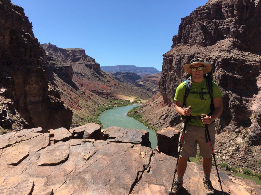 A man with a backpack is standing on a rock near a river