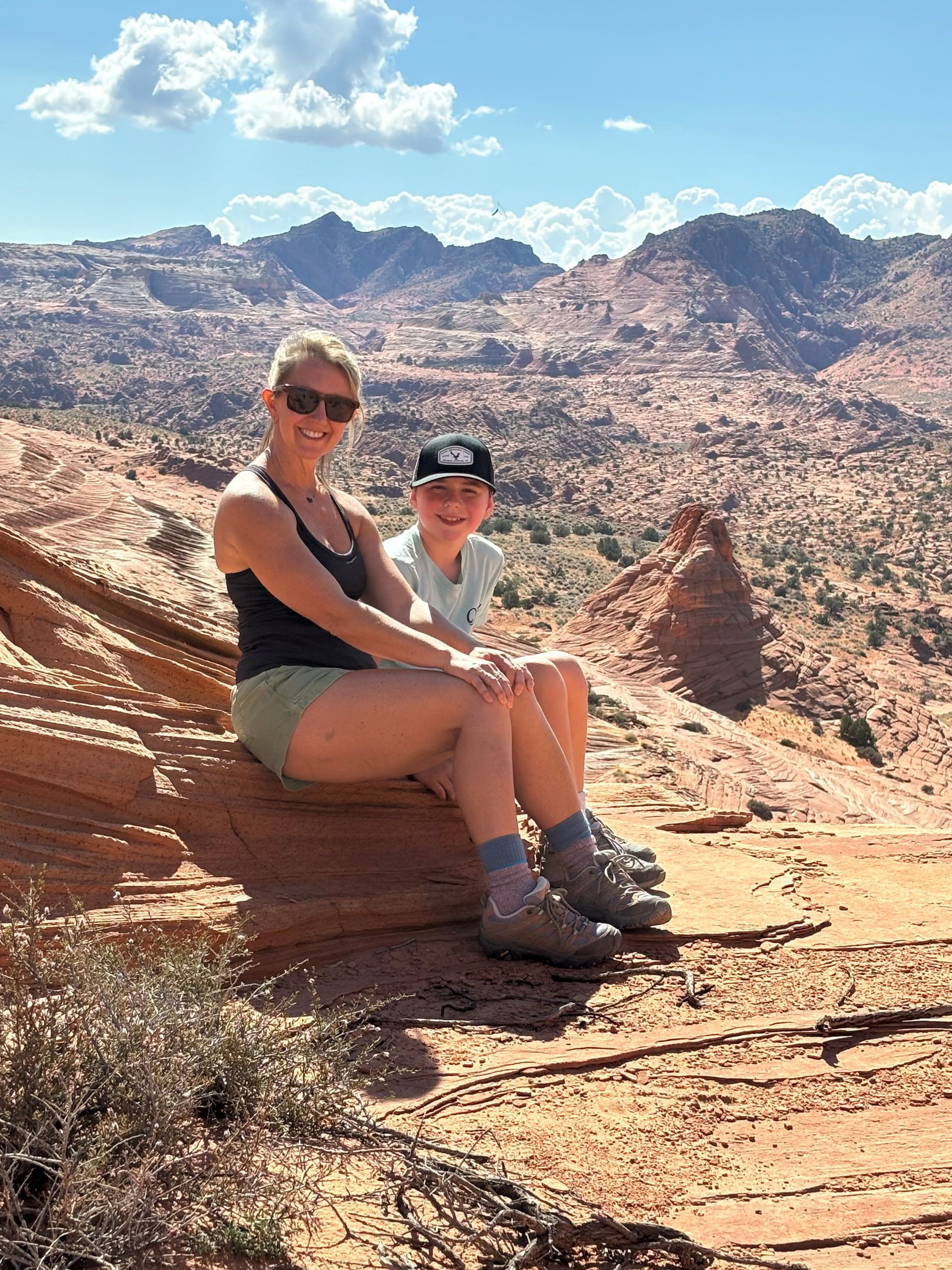 Woman and child sit on red rock outcrop, mountains in the background.