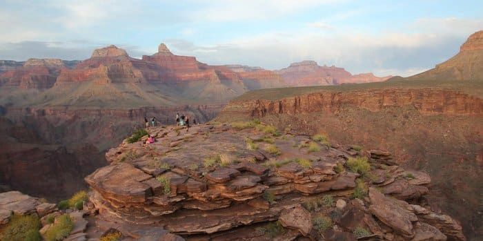 A group of people standing on top of a rocky cliff overlooking a canyon.