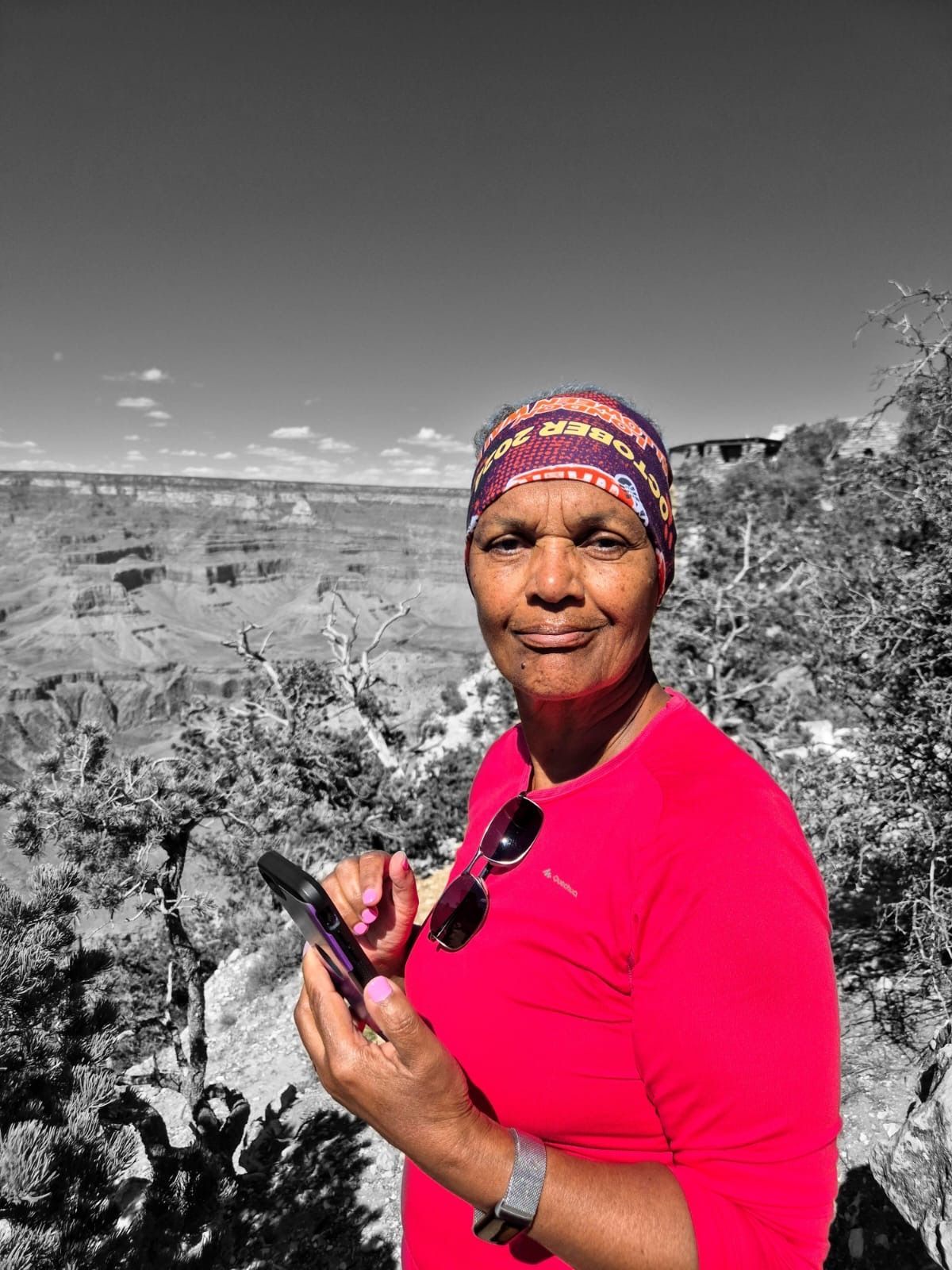 Woman in pink shirt and headscarf holds phone, Grand Canyon in background, colorized.