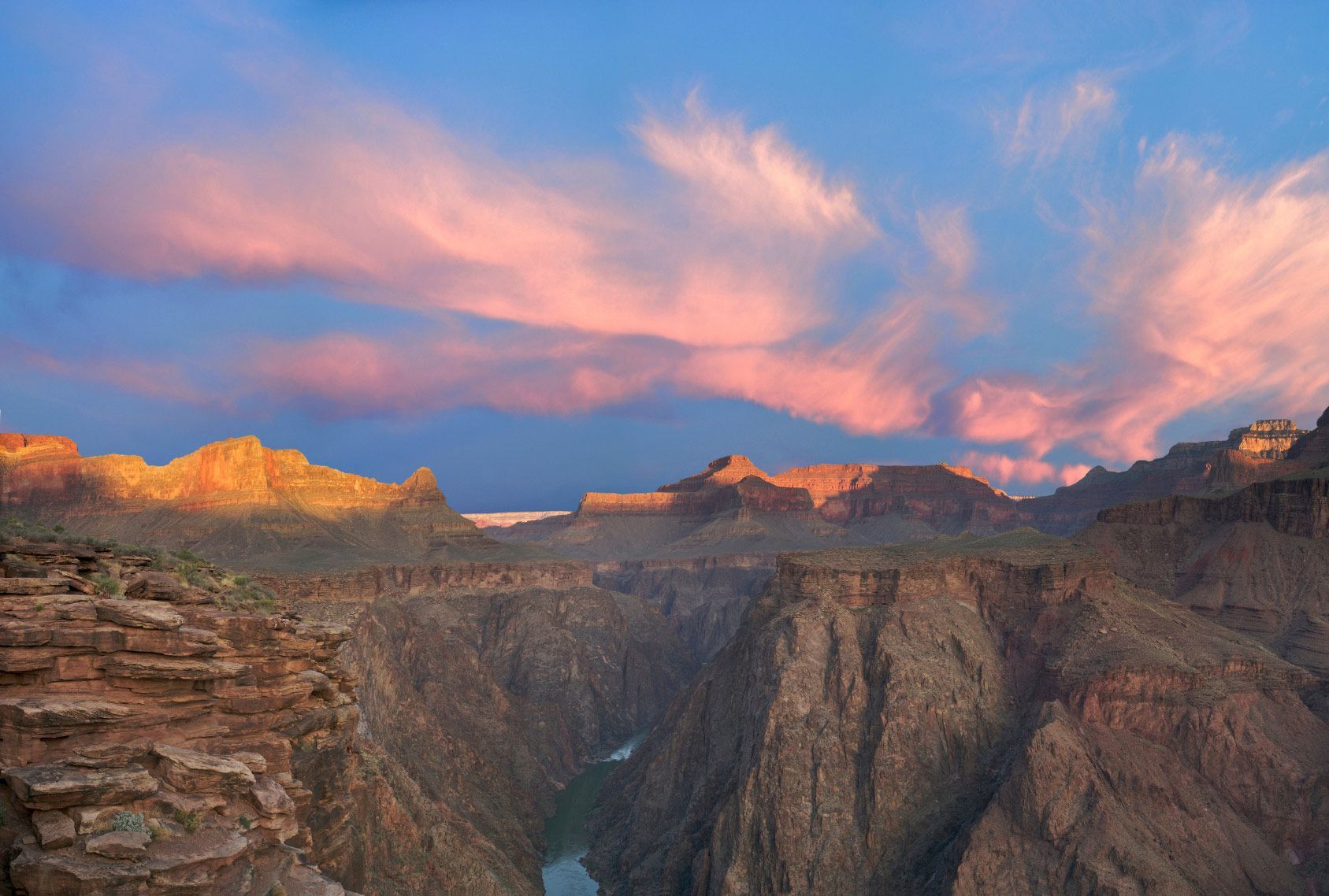 A sunset over a canyon with mountains in the background and a river in the foreground.