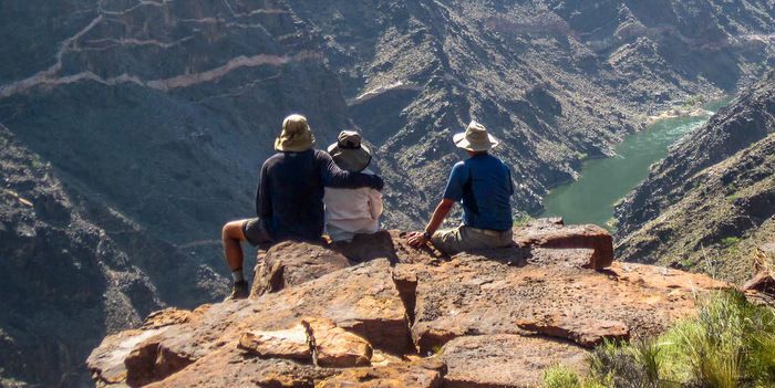 Three people are sitting on a rock overlooking a canyon.