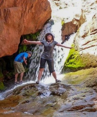 A woman standing in front of a waterfall with her arms outstretched