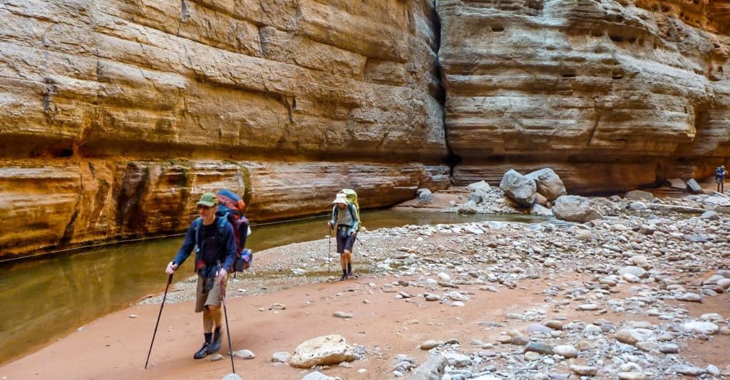 Two people are hiking in a canyon next to a river.