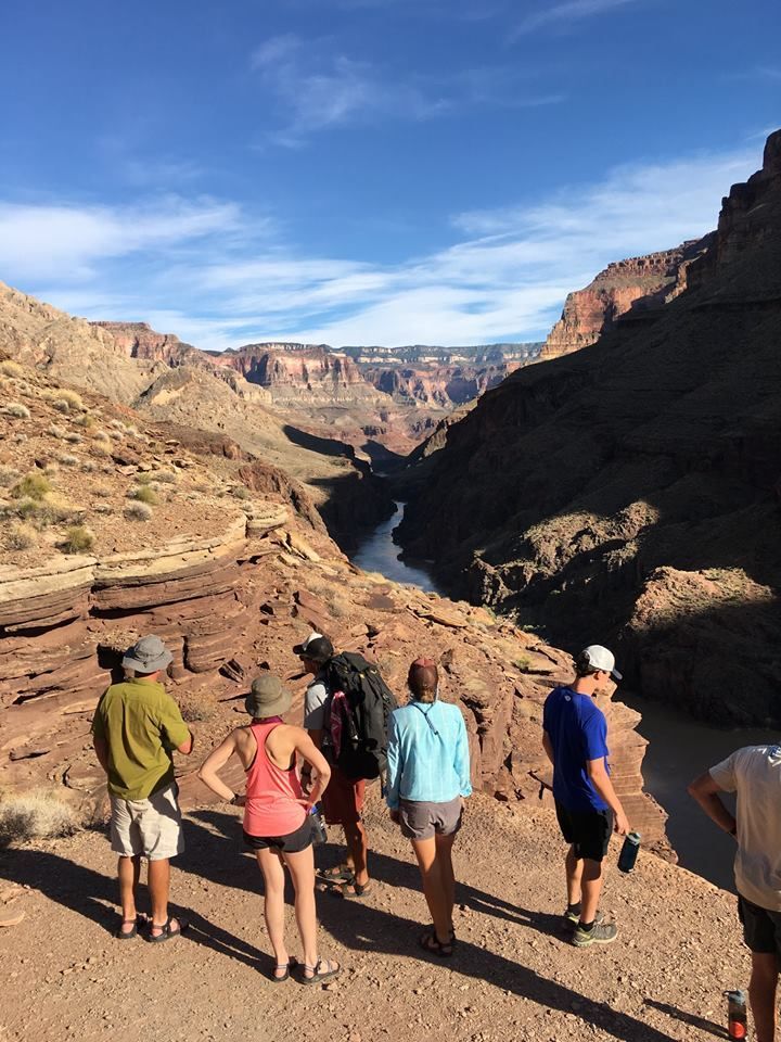 A group of people are standing on top of a rocky hill overlooking a river.