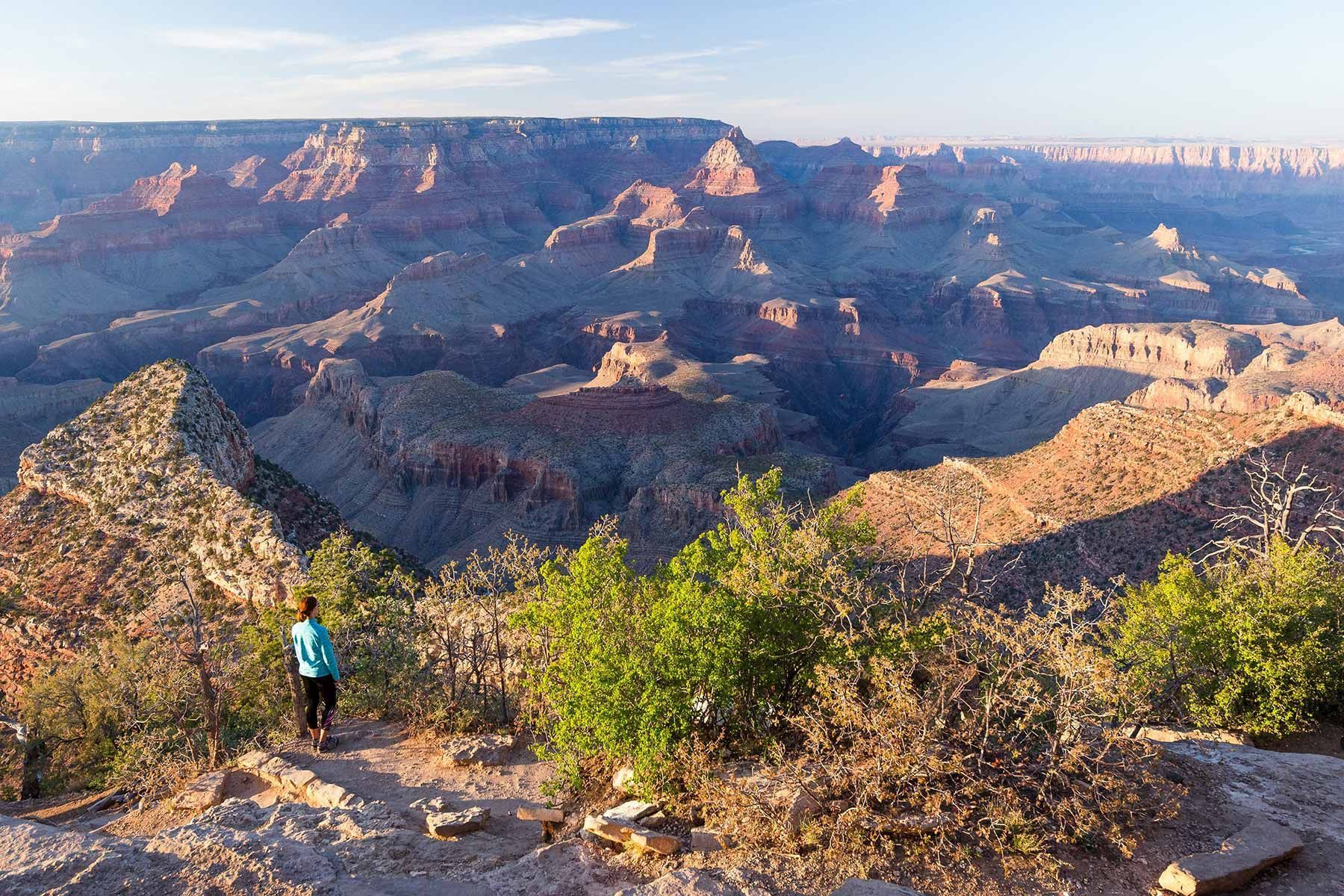 Woman standing at Grand Canyon viewpoint, overlooking vast canyon landscape.