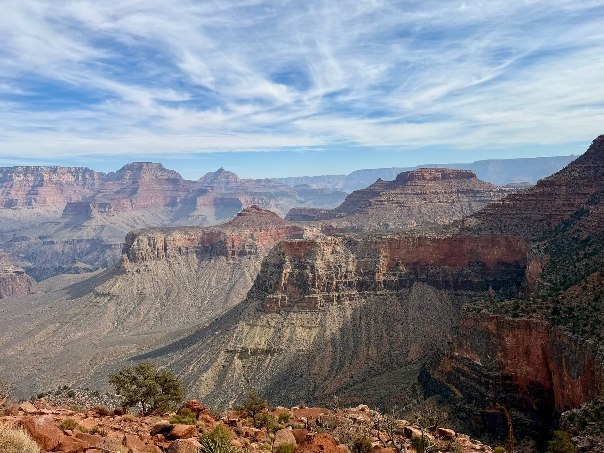 Vast canyon landscape with layered red rock formations under a cloudy blue sky.