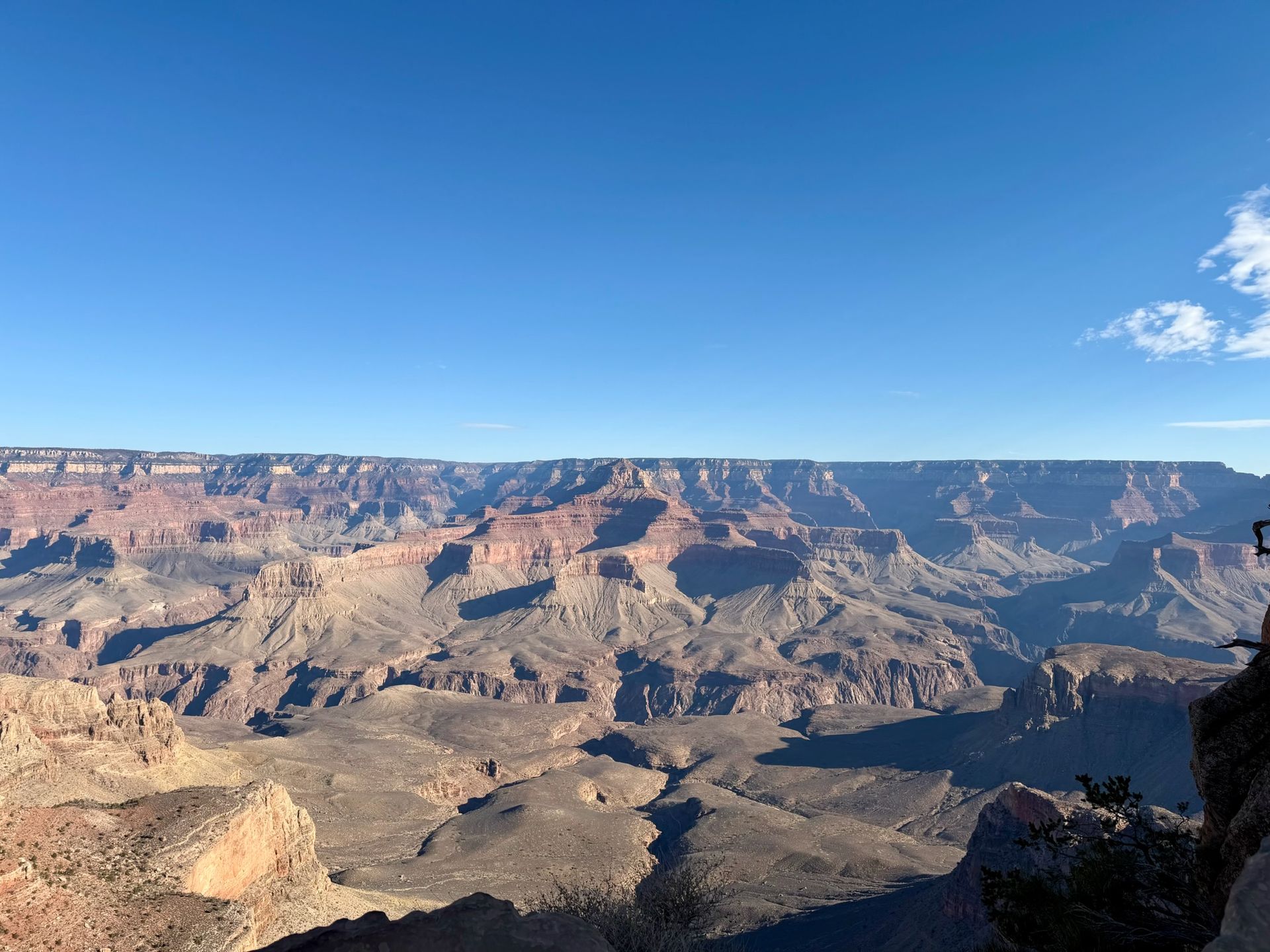 Grand Canyon landscape under a bright blue sky. Red and brown rock formations in the distance.