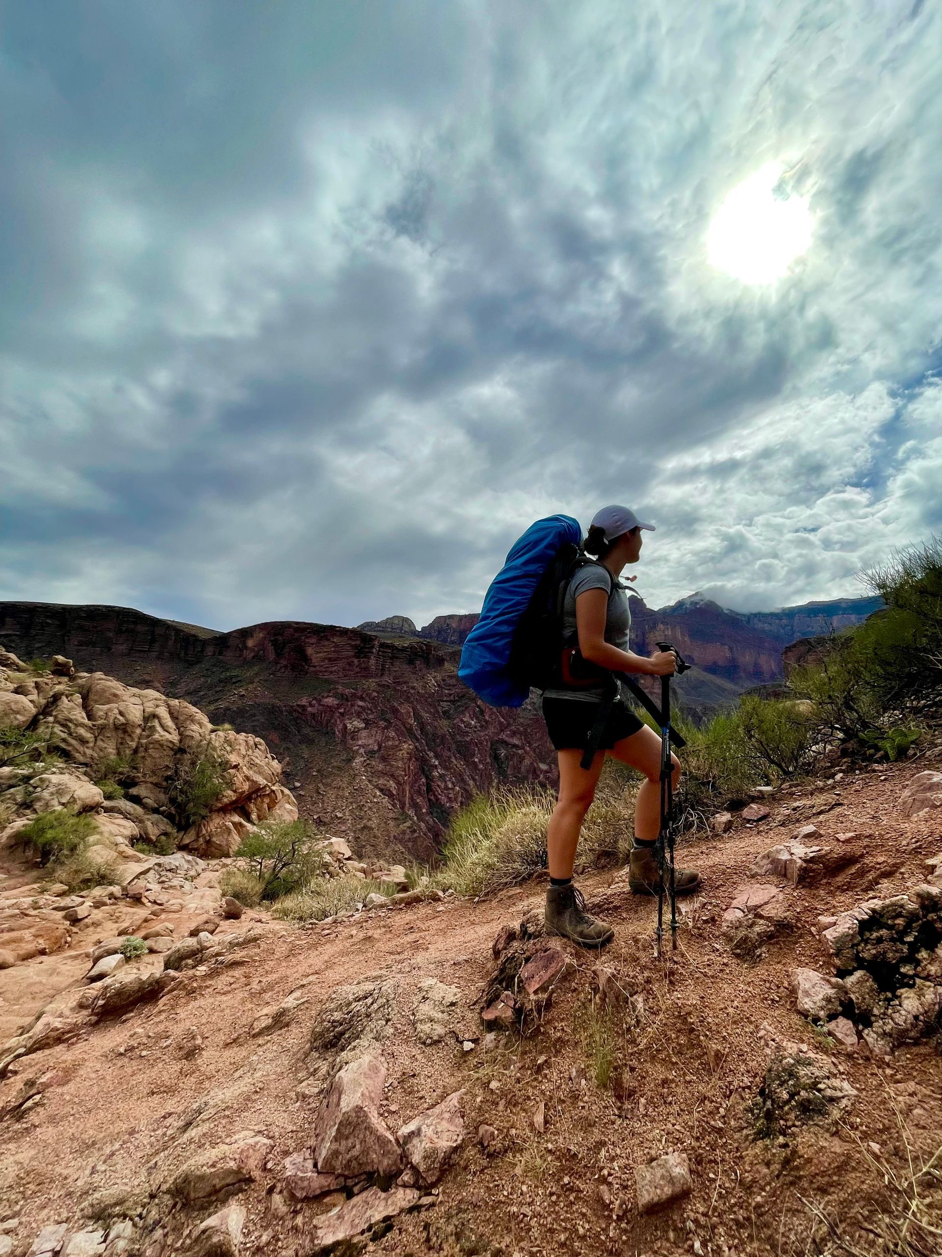 A woman with a backpack and hiking poles is standing on top of a rocky hill.