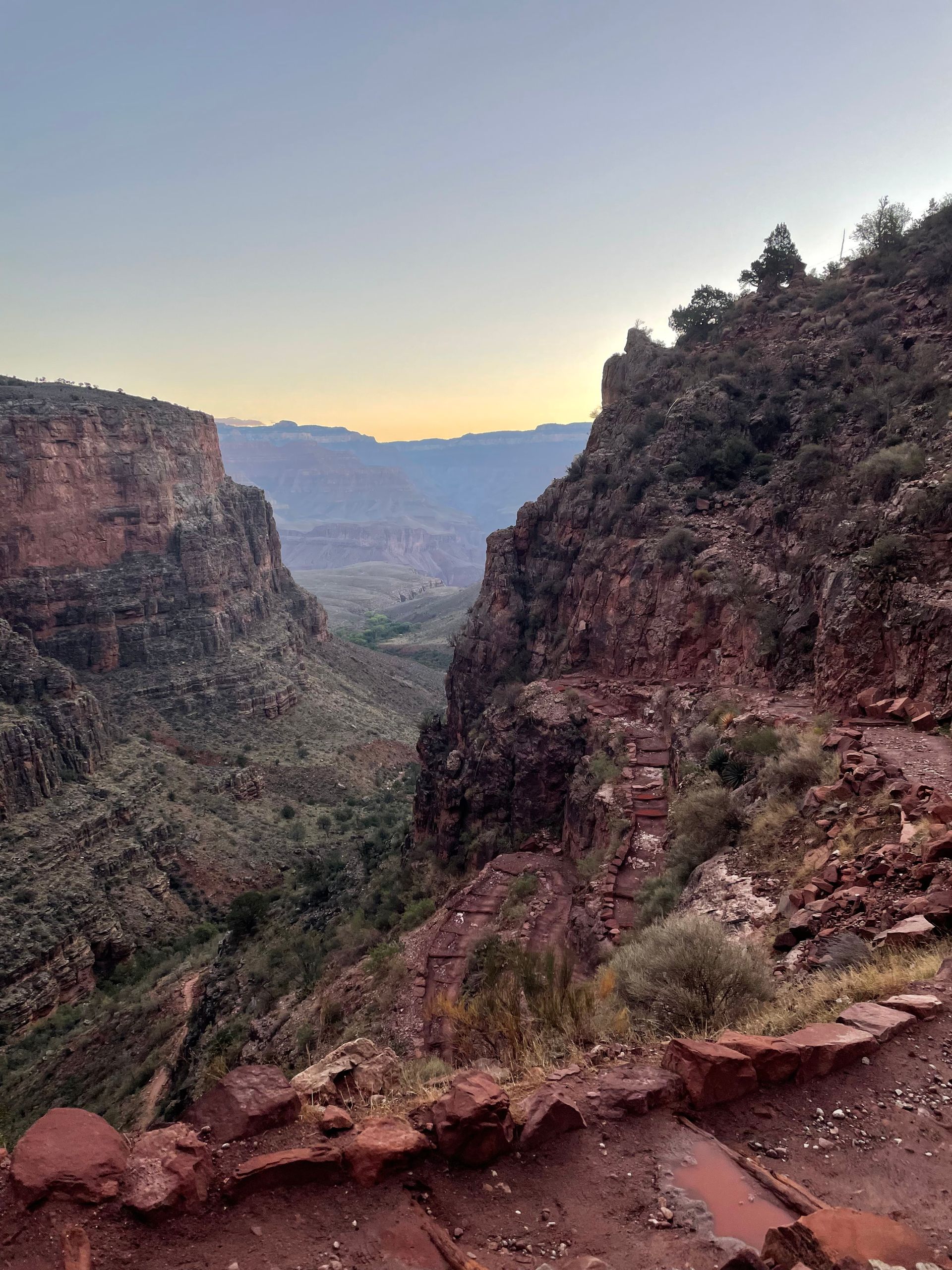 A view of a canyon with mountains in the background at sunset.