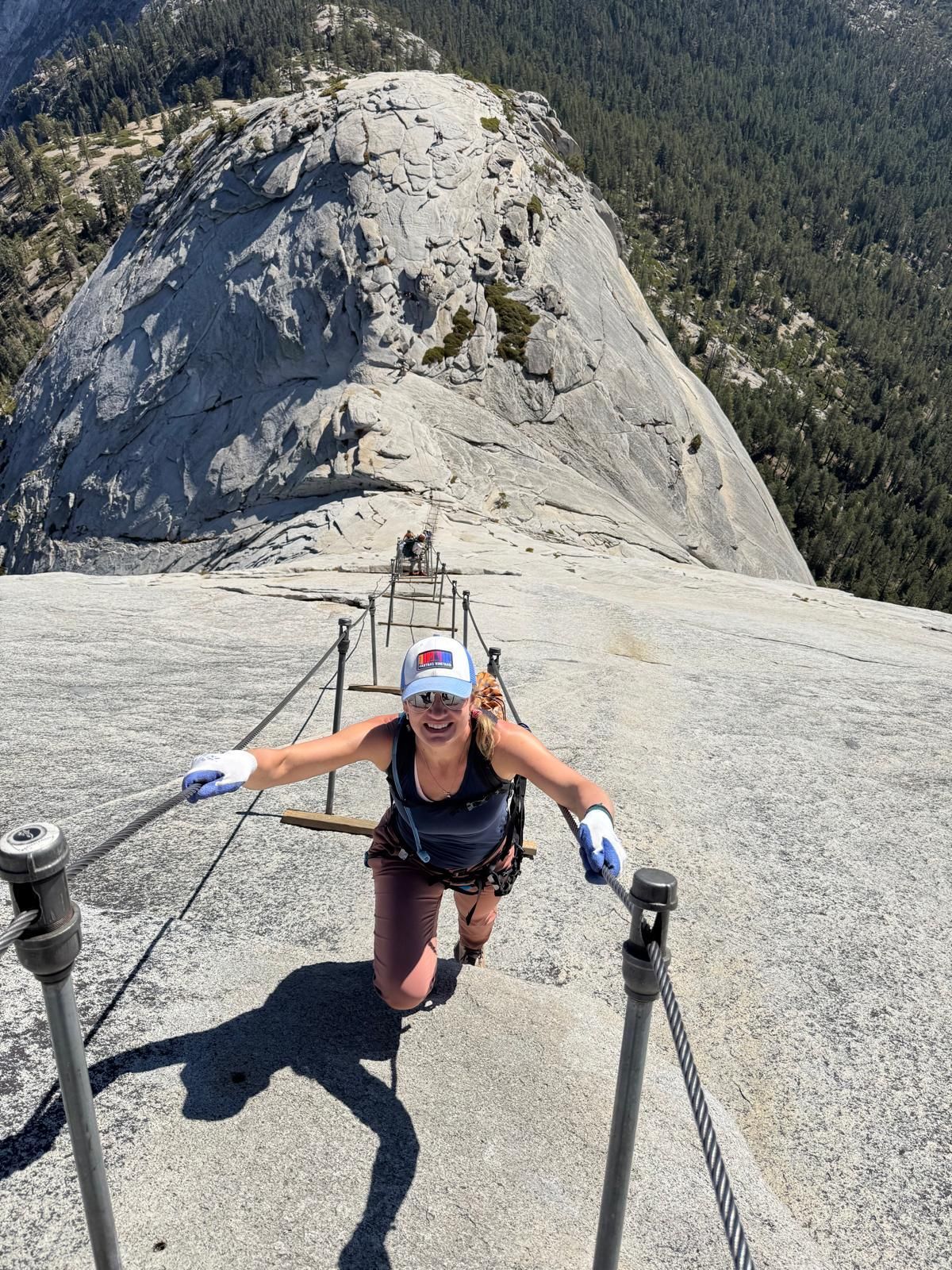 Woman climbing Half Dome cables in Yosemite National Park, sunny day.