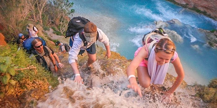 A group of people are hiking up a cliff next to a river.