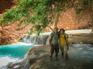 A man and a woman are standing in front of a waterfall.