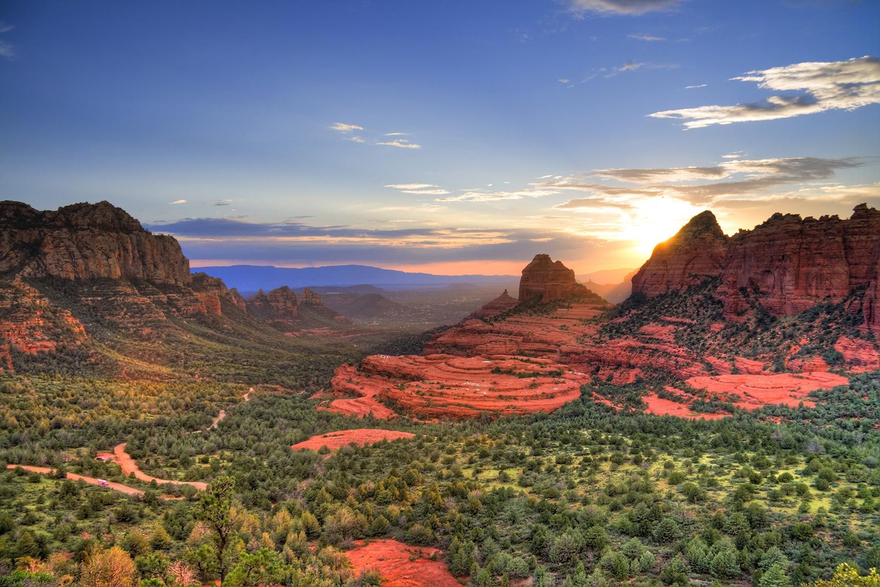 The sun is setting over a valley with mountains in the background.