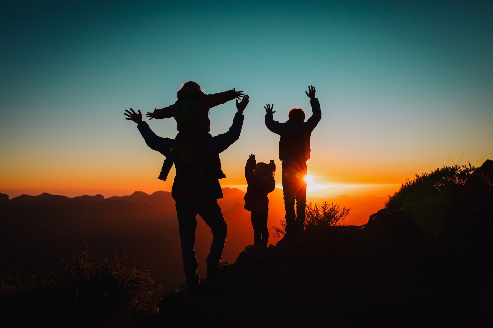 Family silhouetted against a sunset, celebrating on a mountaintop.