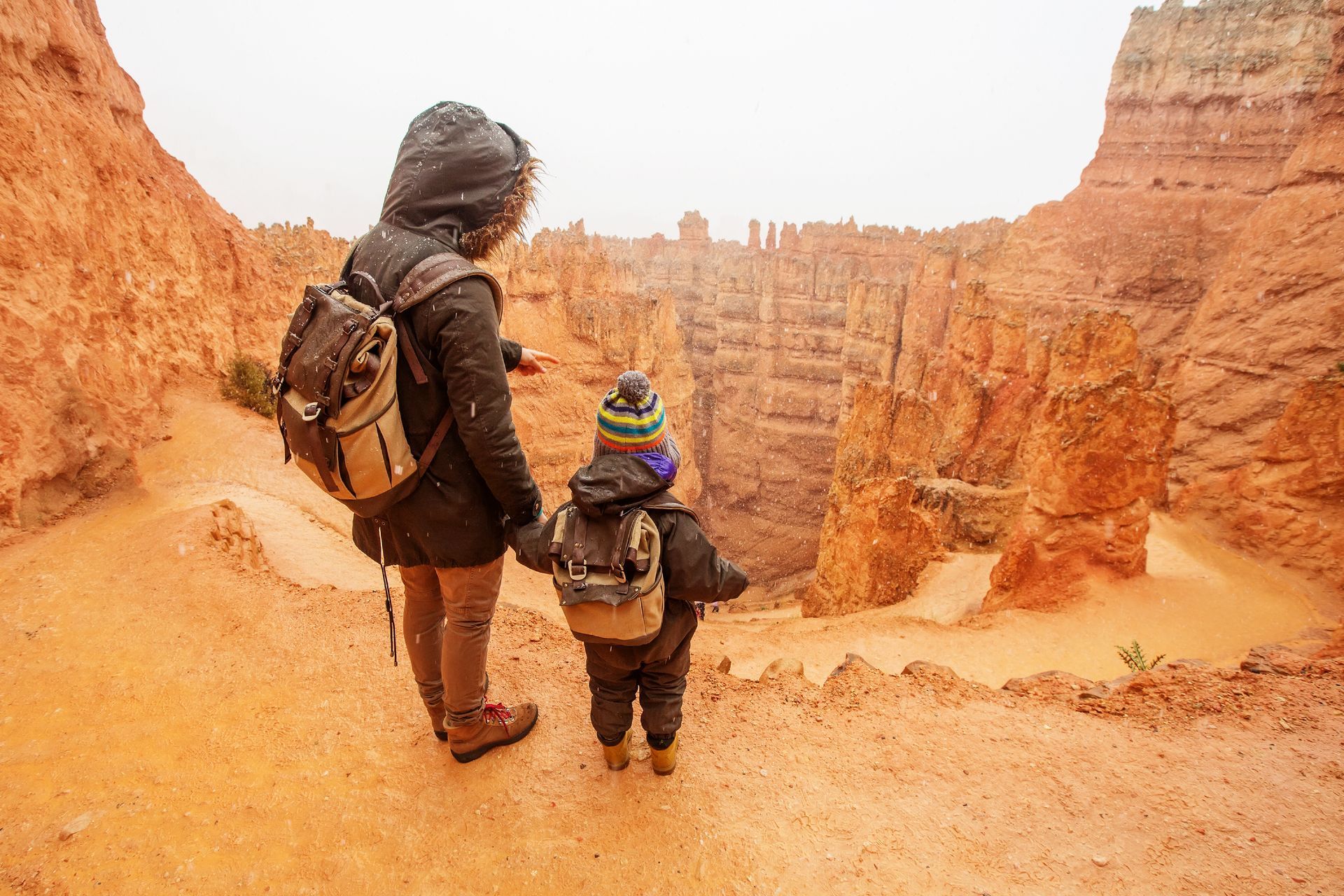 Mother and child in winter gear holding hands, looking at orange canyon.