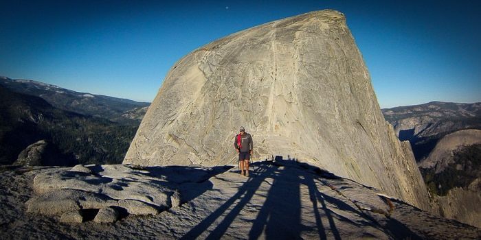 A man with a backpack is standing on top of a large rock.