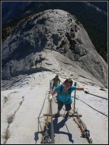 A man is walking up a rope bridge on top of a mountain.