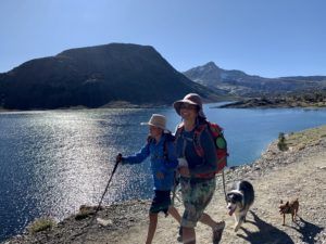 A woman and a child are hiking with a dog near a lake.