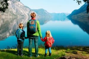 A woman and two children are standing next to a lake holding hands.