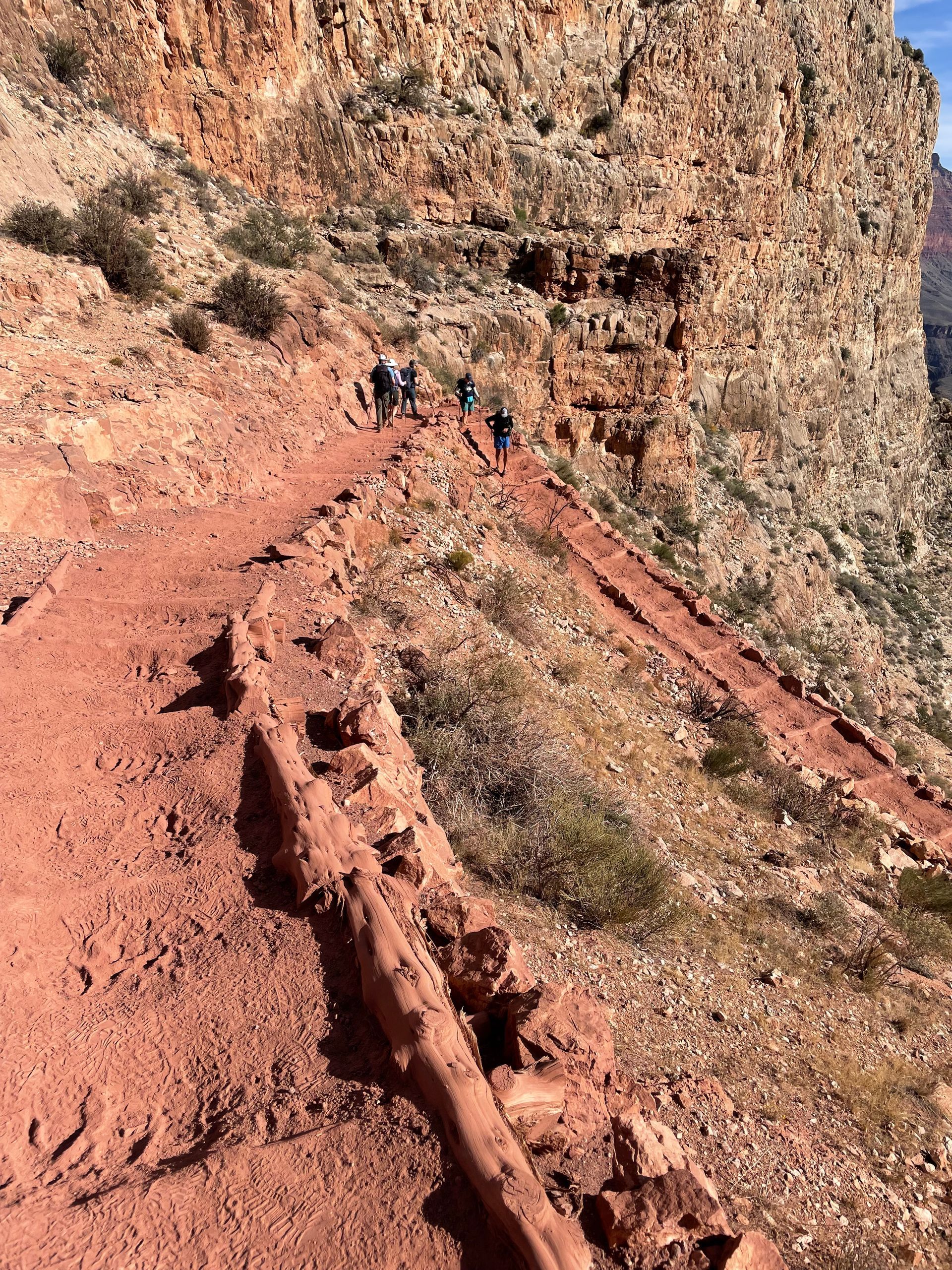 A group of people are walking down a dirt path in the mountains.