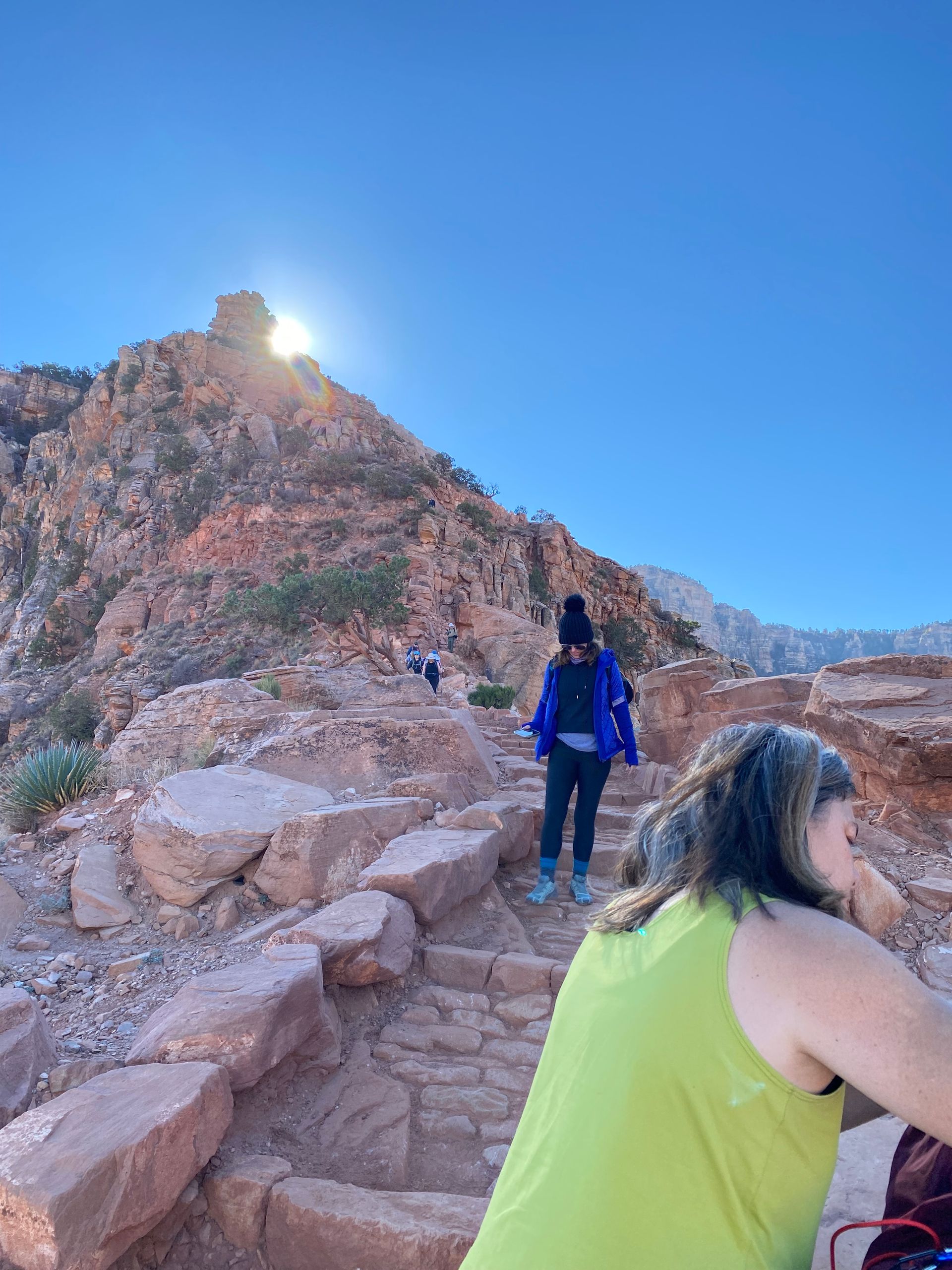 A woman in a green tank top is sitting on a rocky hillside.