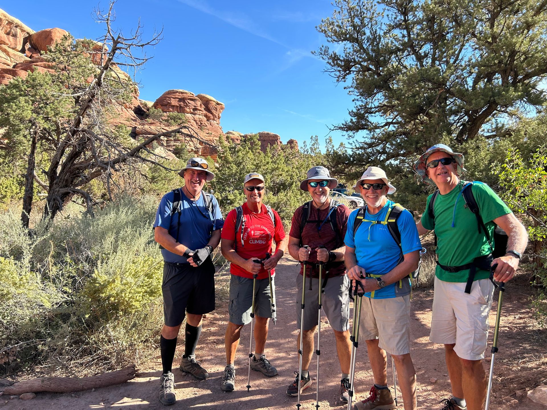 A group of men are standing next to each other on a trail holding hiking poles.