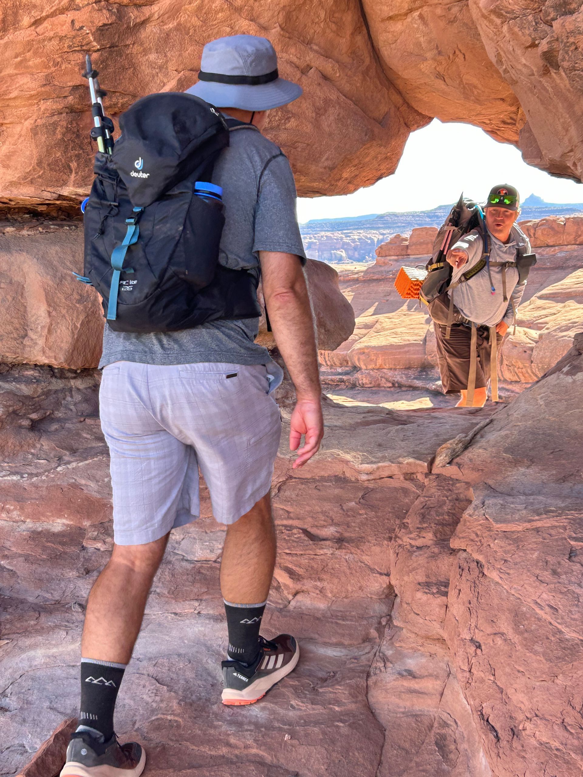 A man with a backpack is walking through a rock archway.