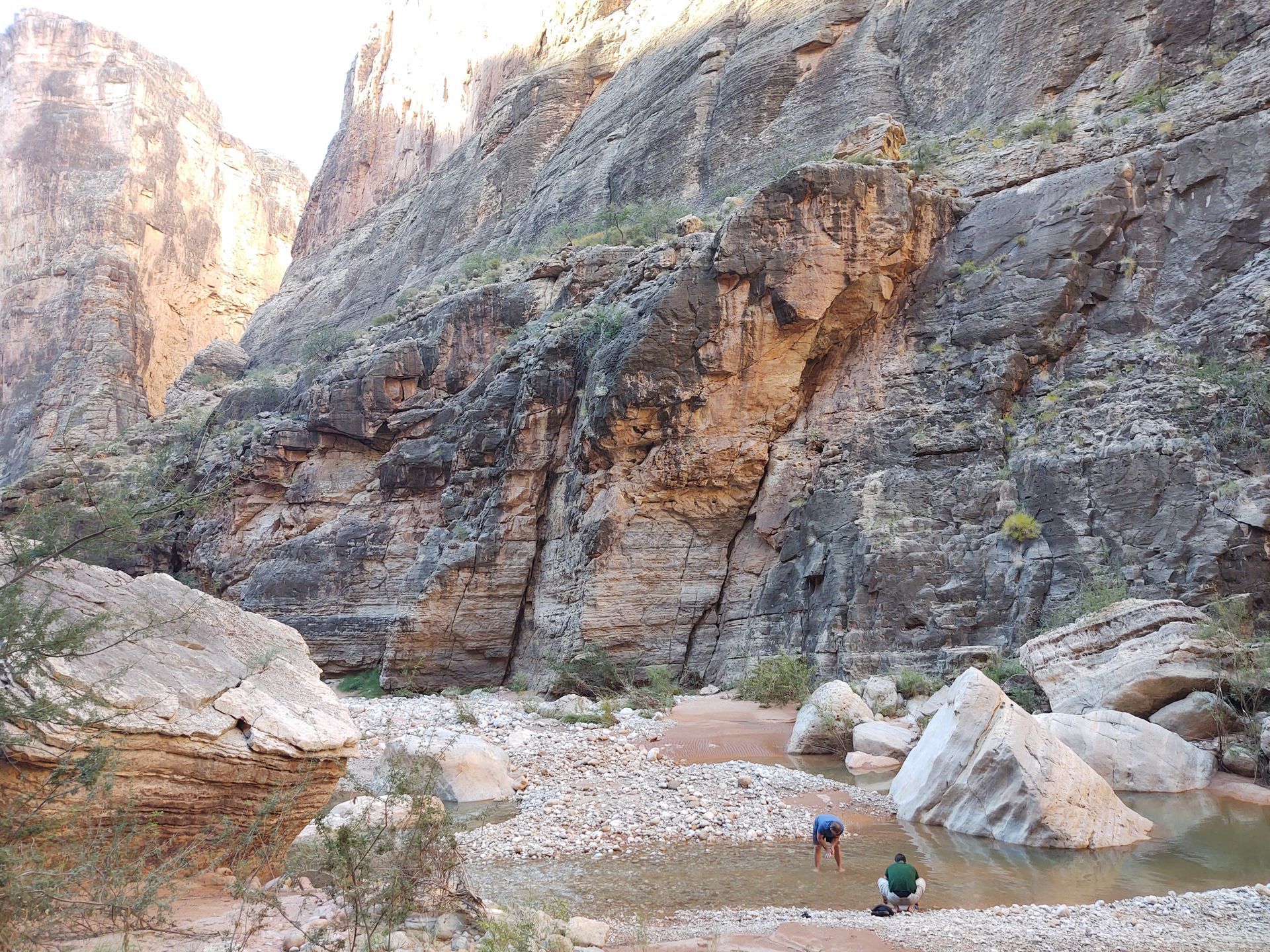 A couple of people standing next to a river in a canyon.