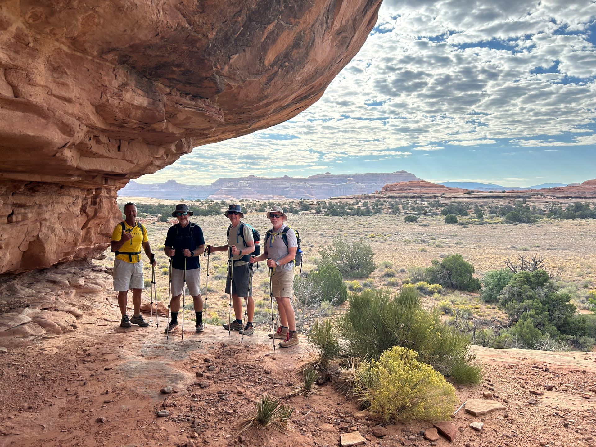 A group of people are standing under a rock in the desert.