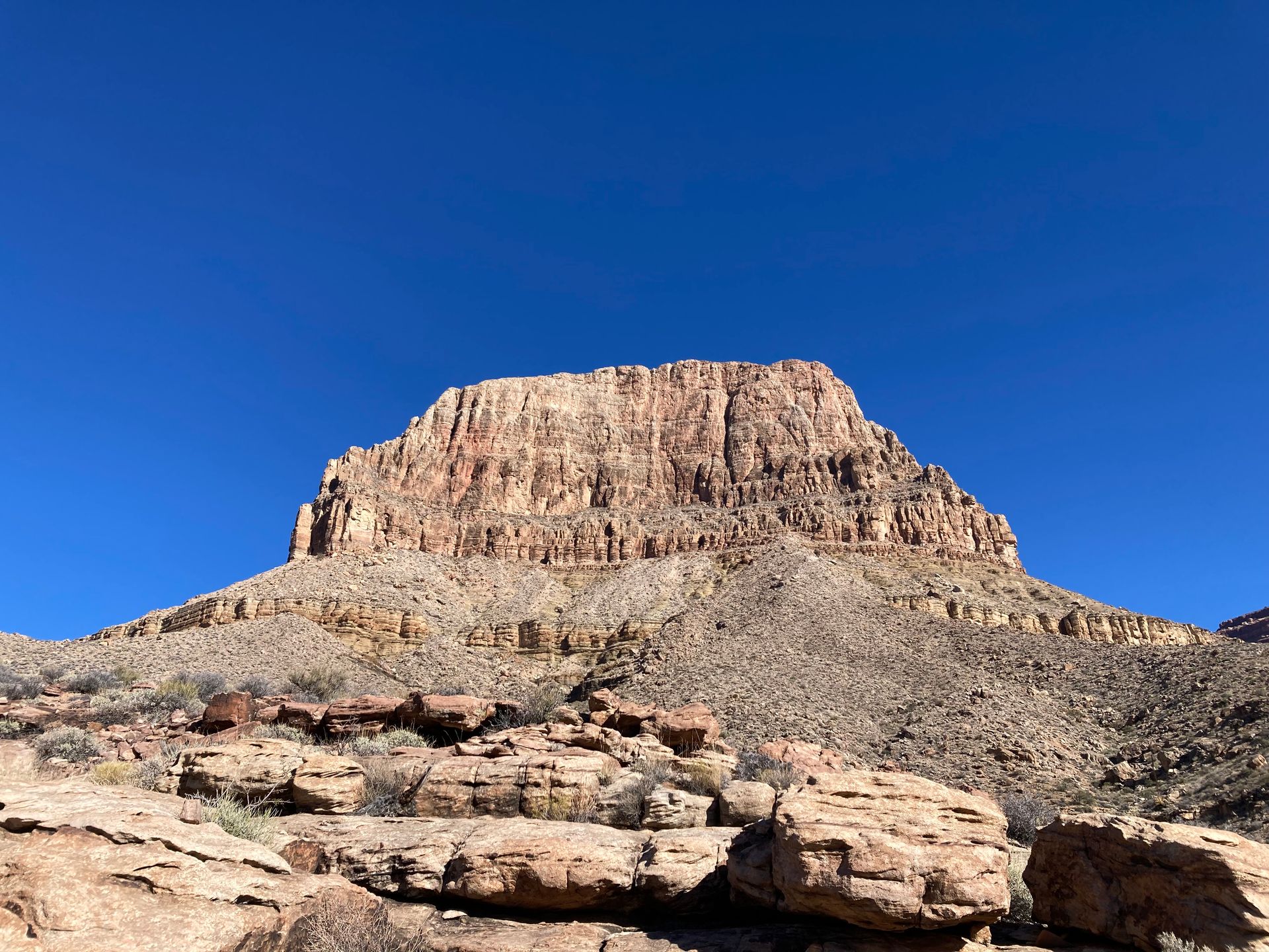A large rocky mountain in the desert with a blue sky in the background.