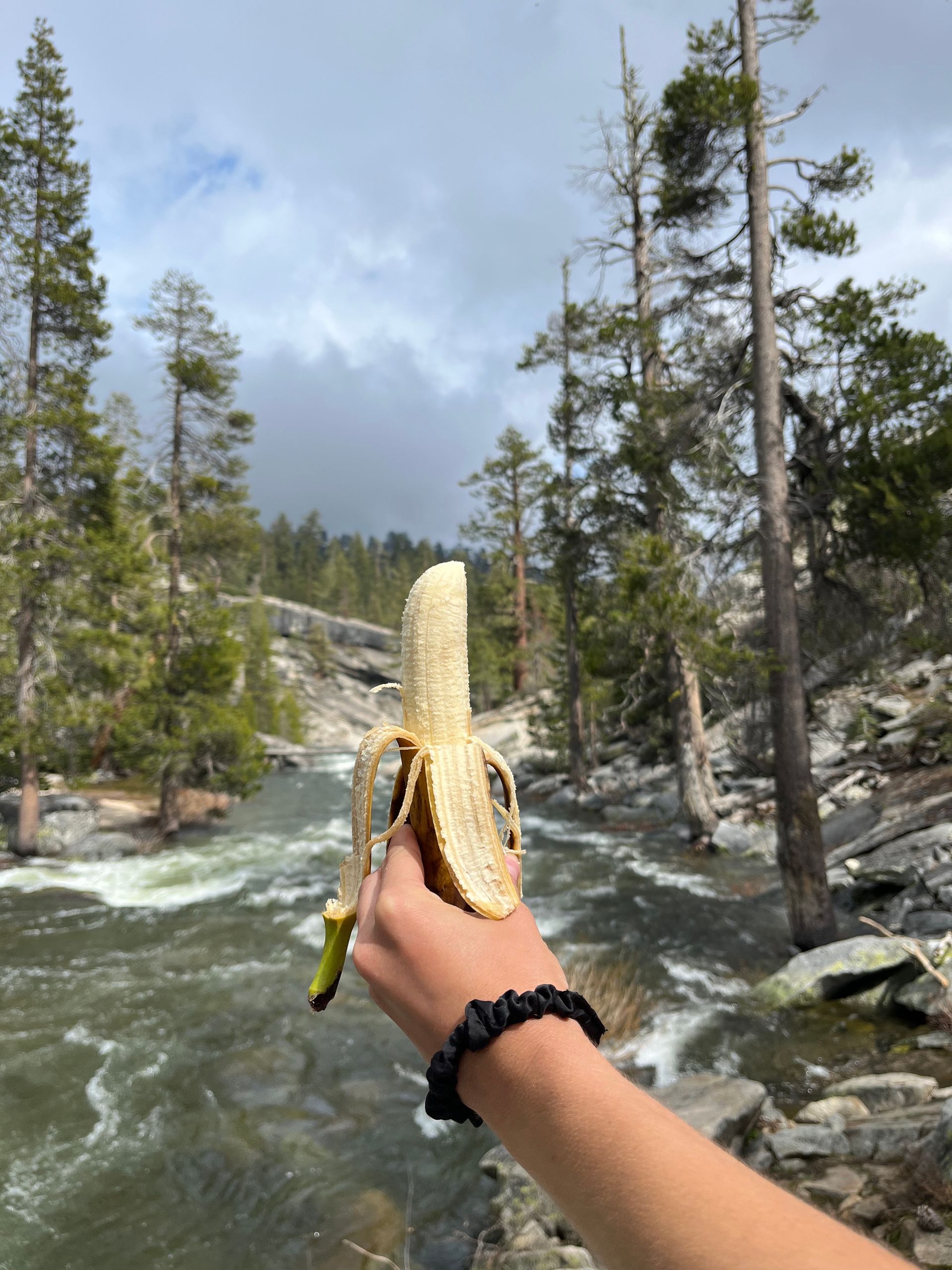 A person is holding a banana in front of a river.