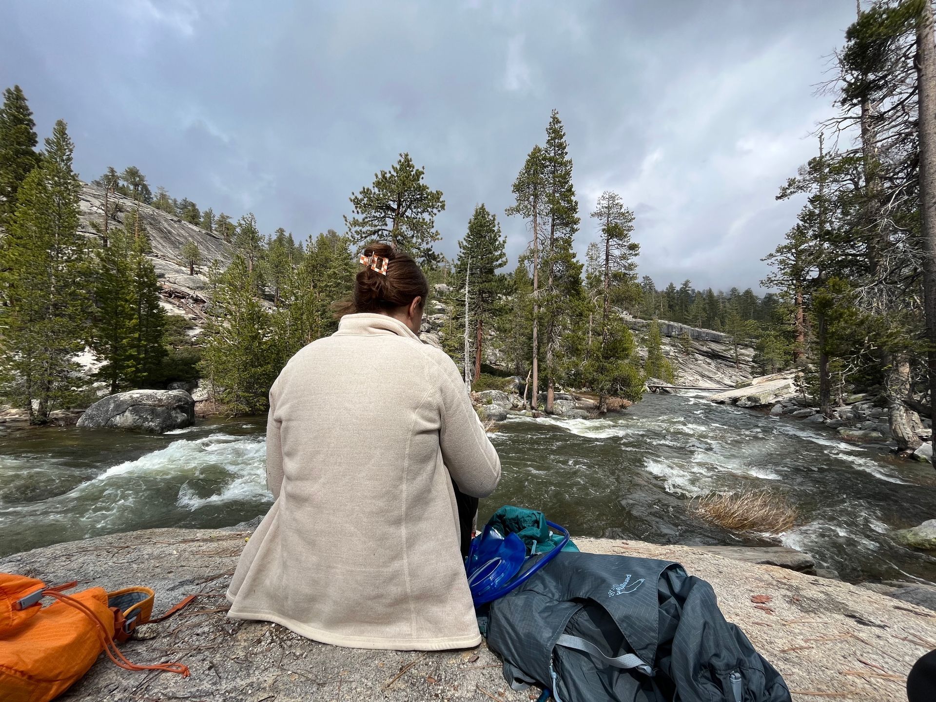 A woman is sitting on a rock overlooking a river.