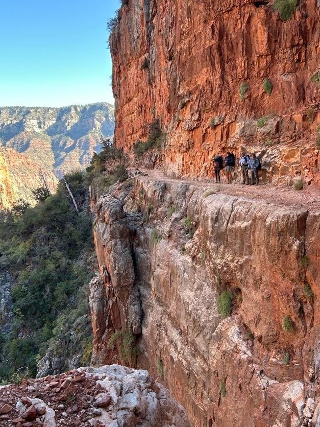 A group of people are walking down a trail on the side of a cliff.