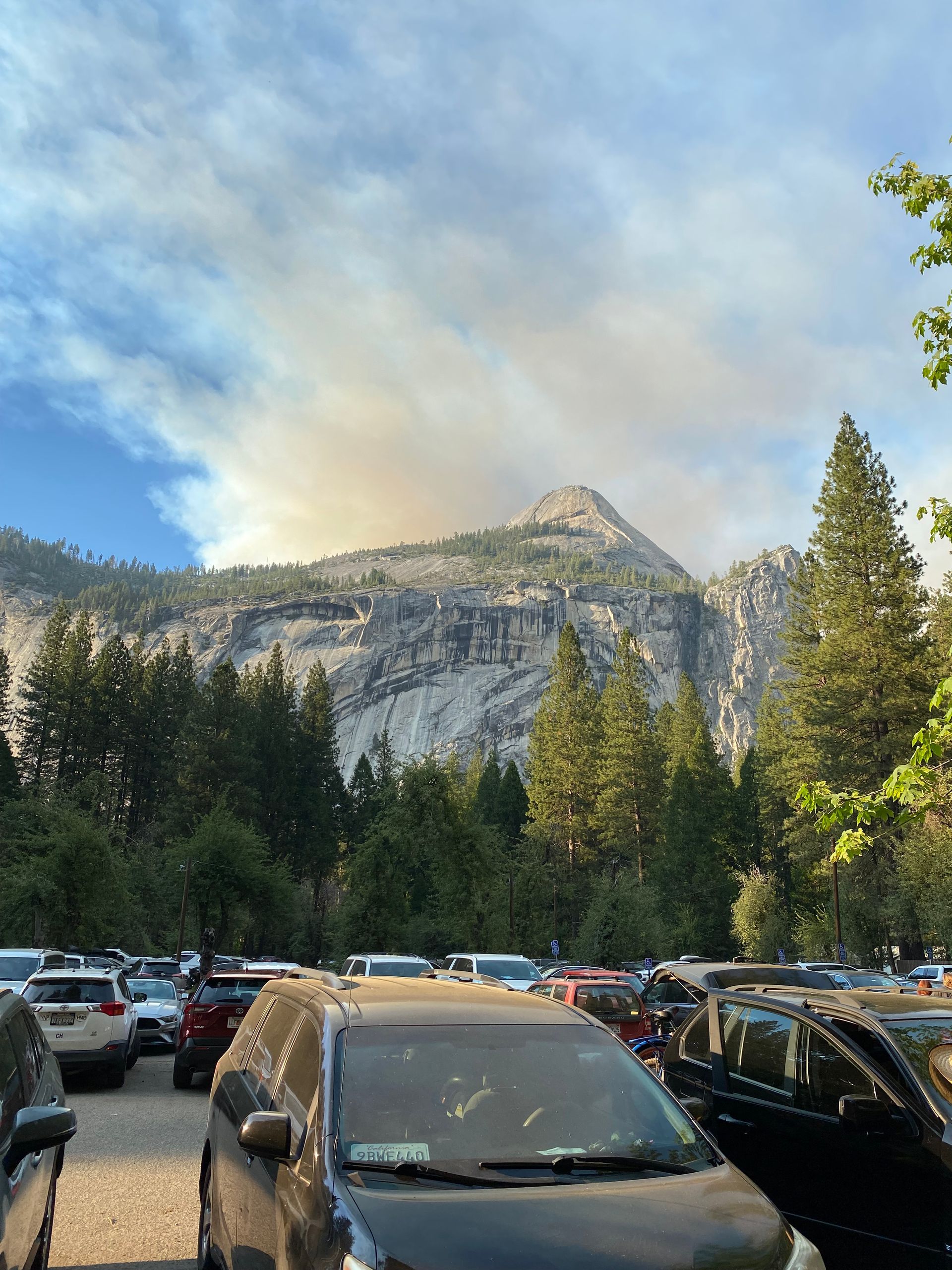 A lot of cars are parked in a parking lot with a mountain in the background.