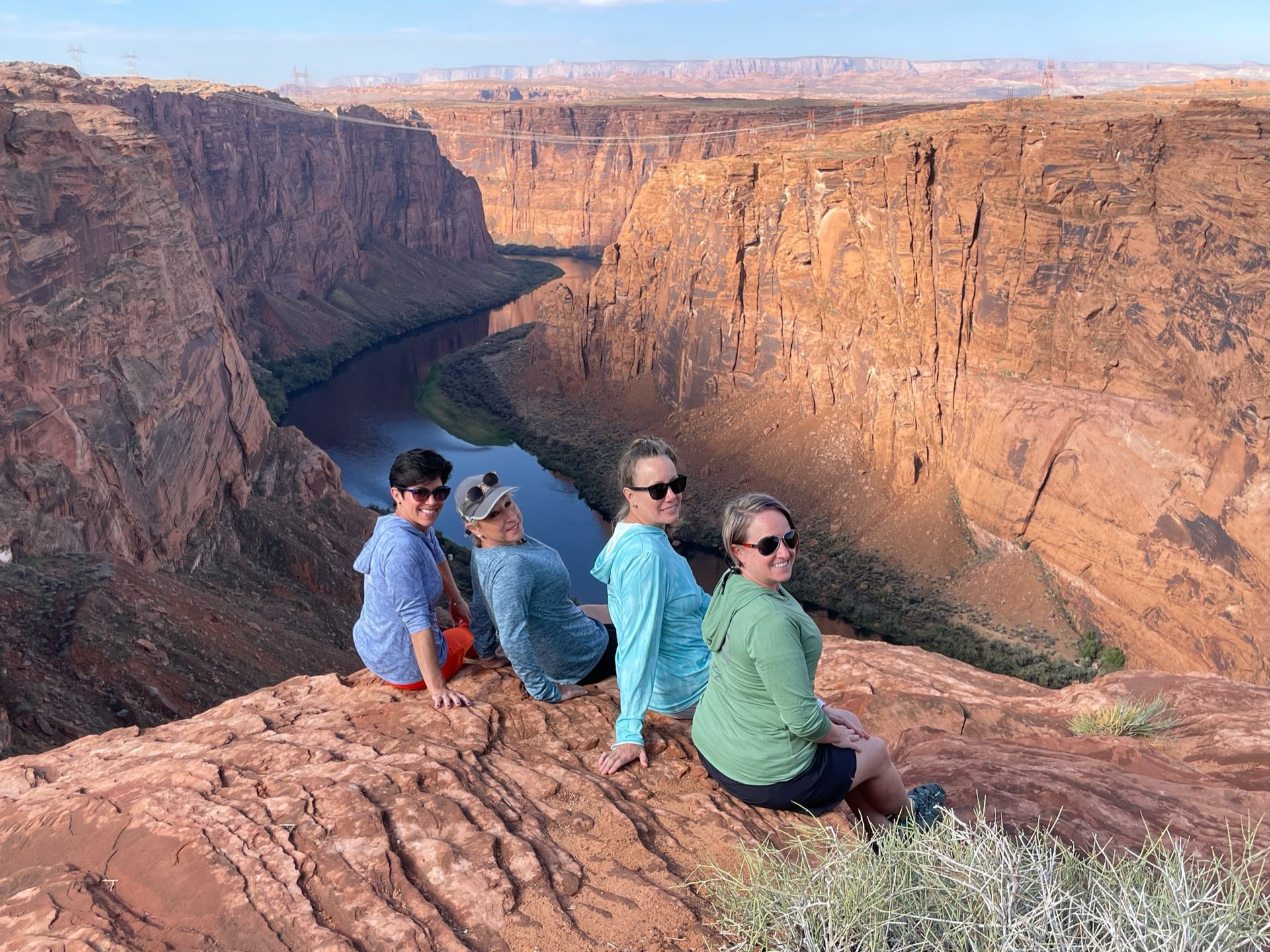 A group of people are sitting on top of a cliff overlooking a river.