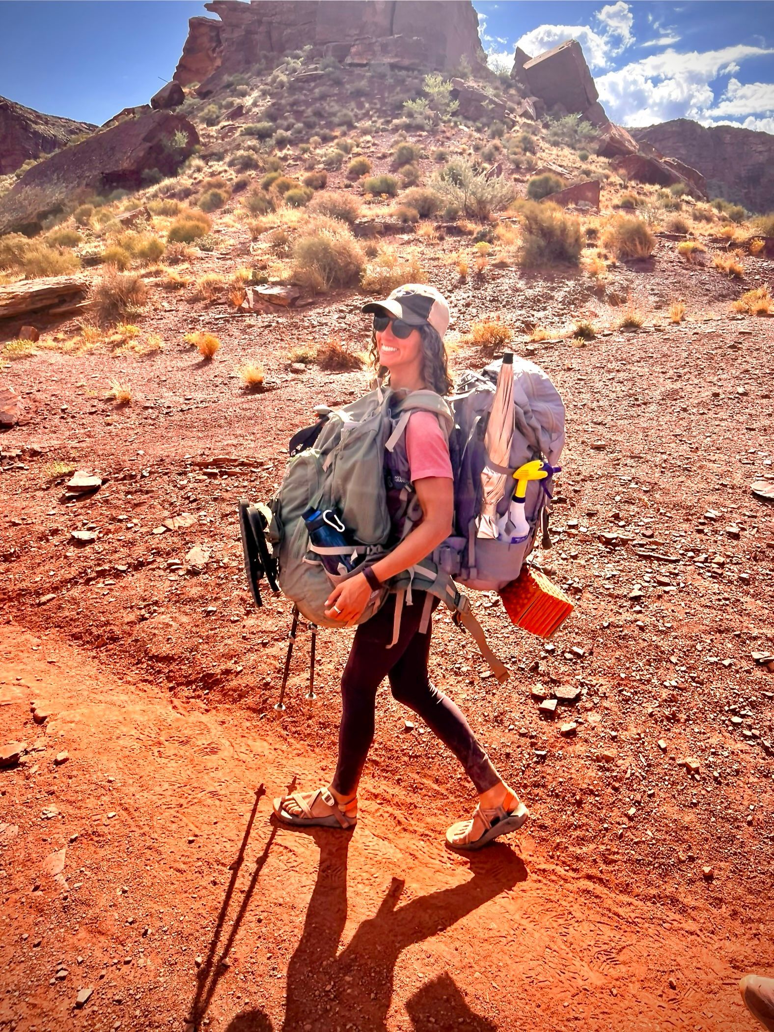 A woman with a backpack is walking on a dirt path in the desert.