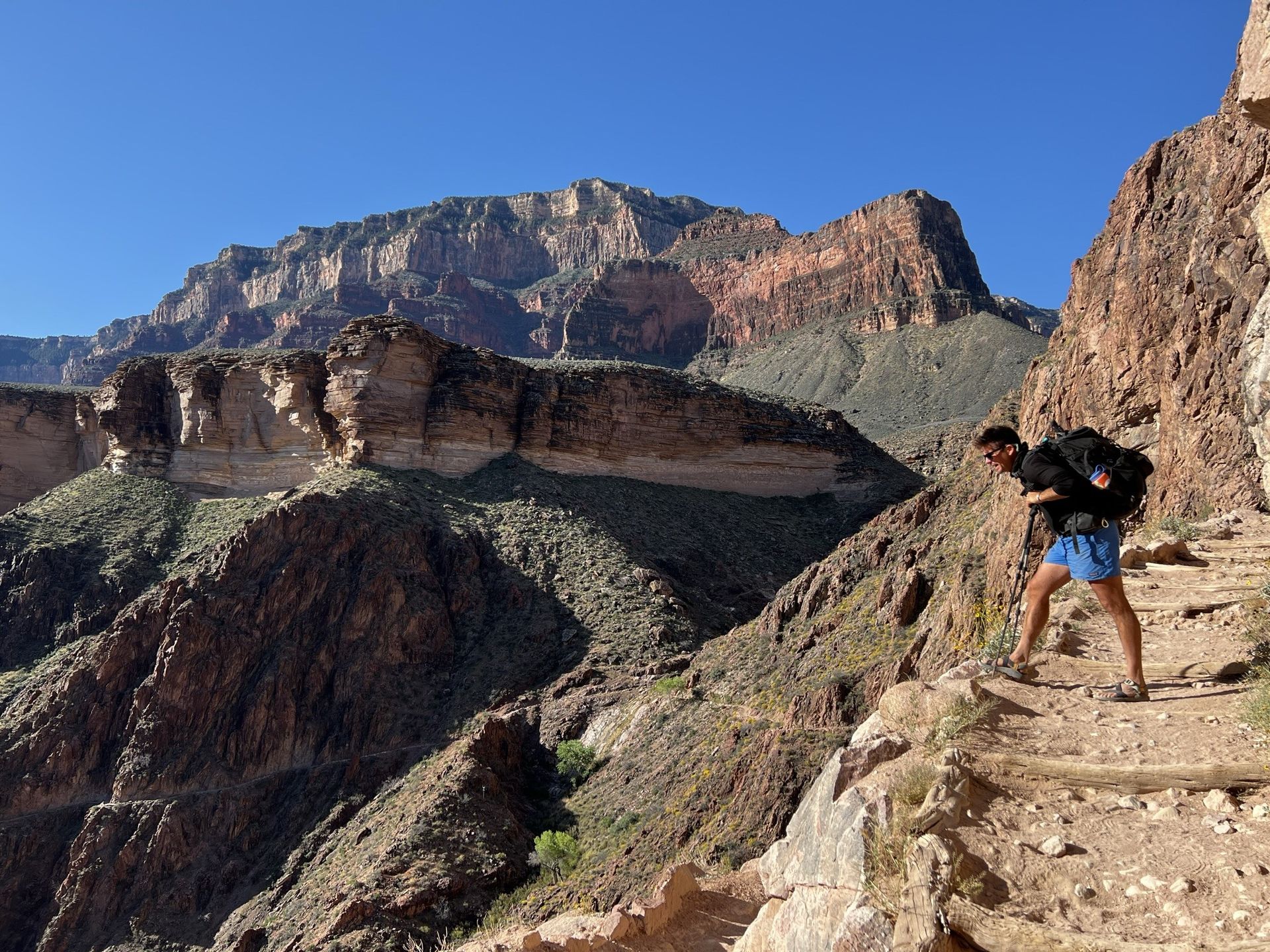 A man with a backpack is walking down a trail in the mountains.