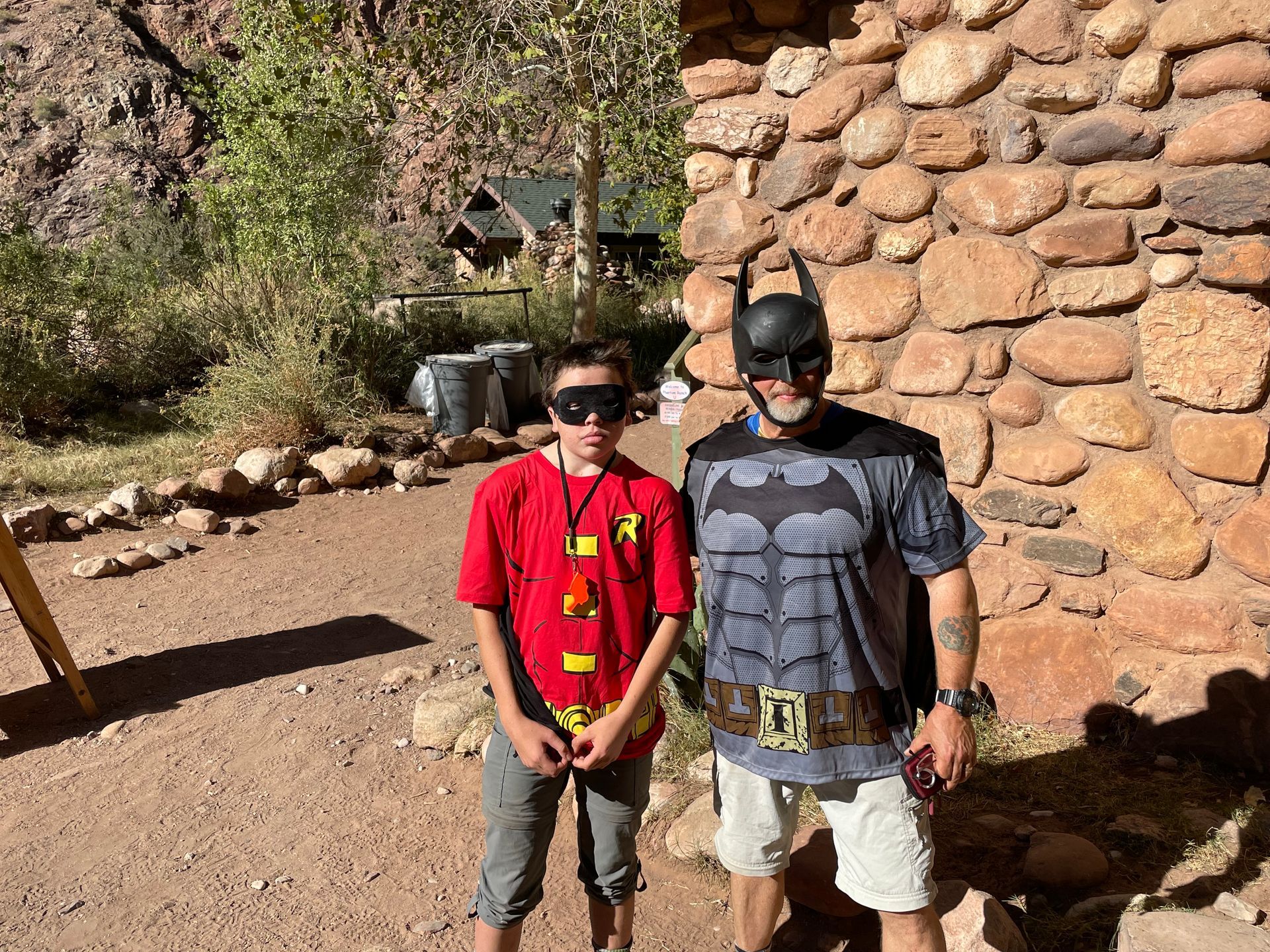 A man and a boy are standing next to each other in front of a stone wall.